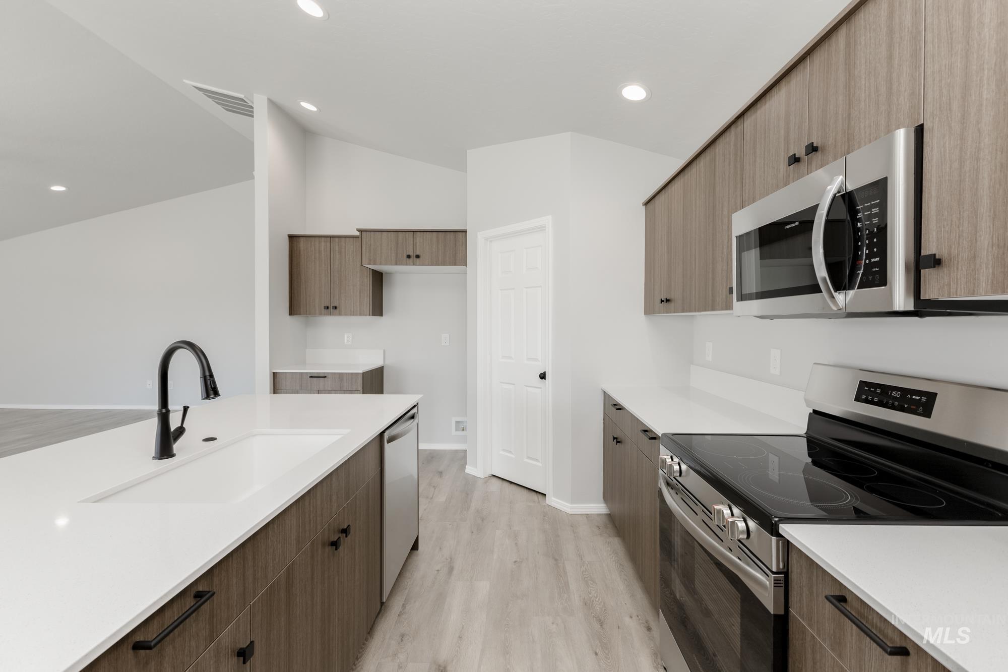 Kitchen featuring appliances with stainless steel finishes, modern cabinets, light wood-style floors, vaulted ceiling, and recessed lighting