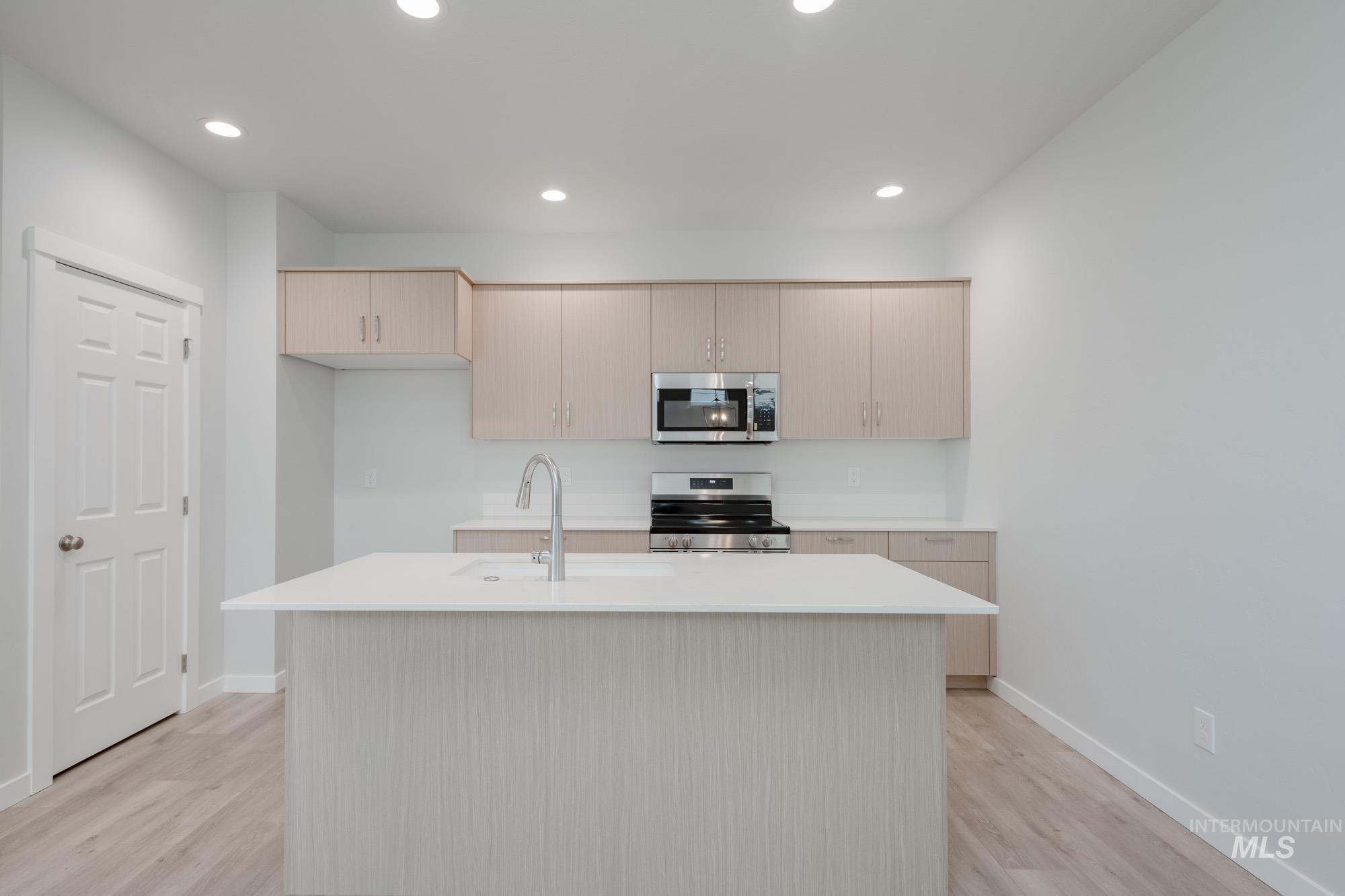 Kitchen featuring stainless steel appliances, light wood-type flooring, recessed lighting, a center island with sink, and light brown cabinets