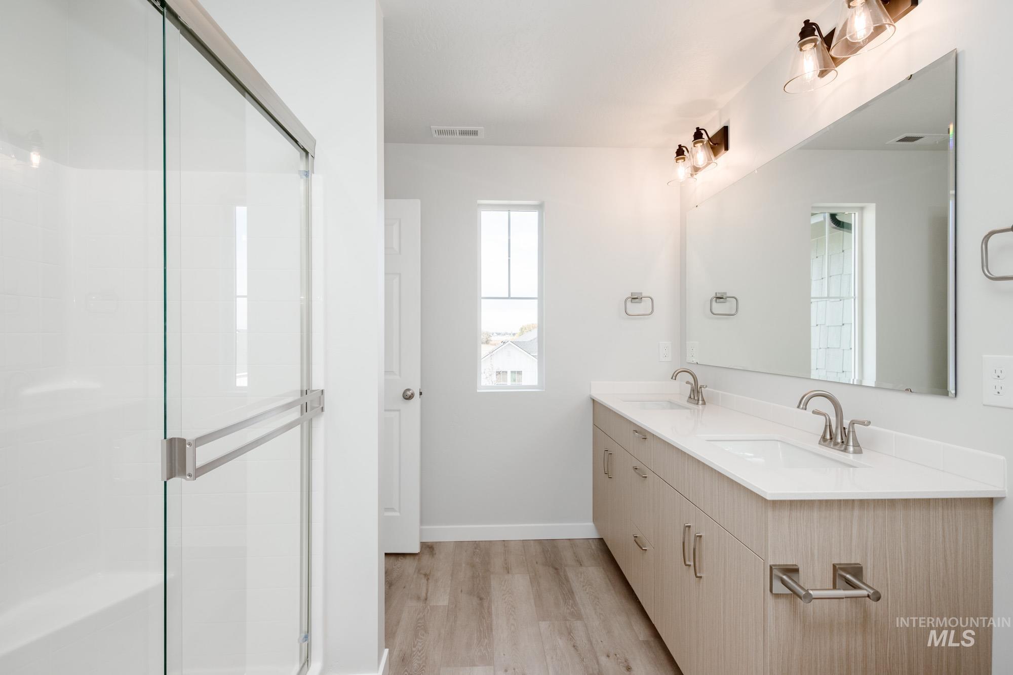Bathroom with double vanity, light wood finished floors, and a shower stall