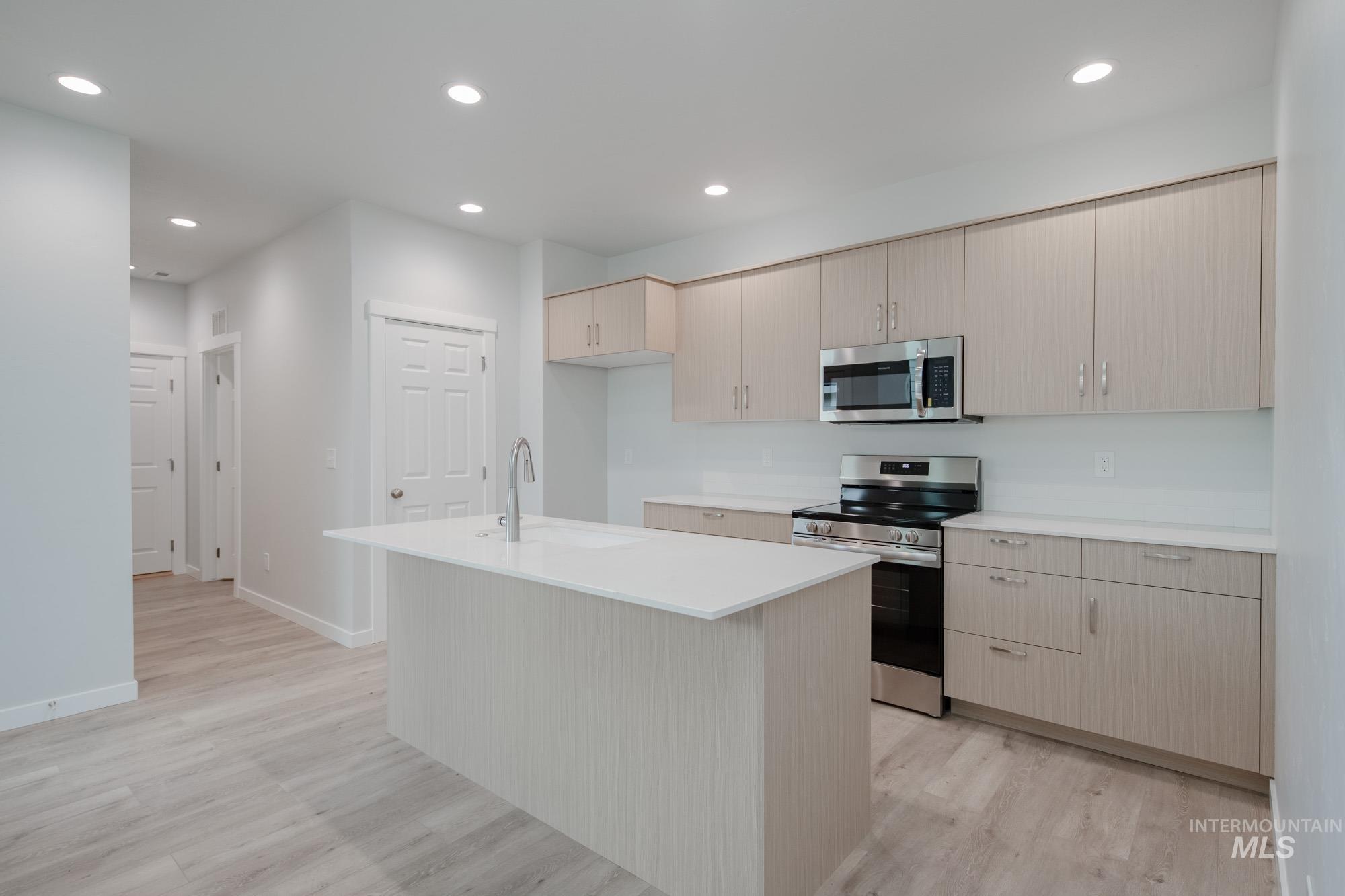 Kitchen with appliances with stainless steel finishes, a kitchen island with sink, light wood-style floors, recessed lighting, and light brown cabinets
