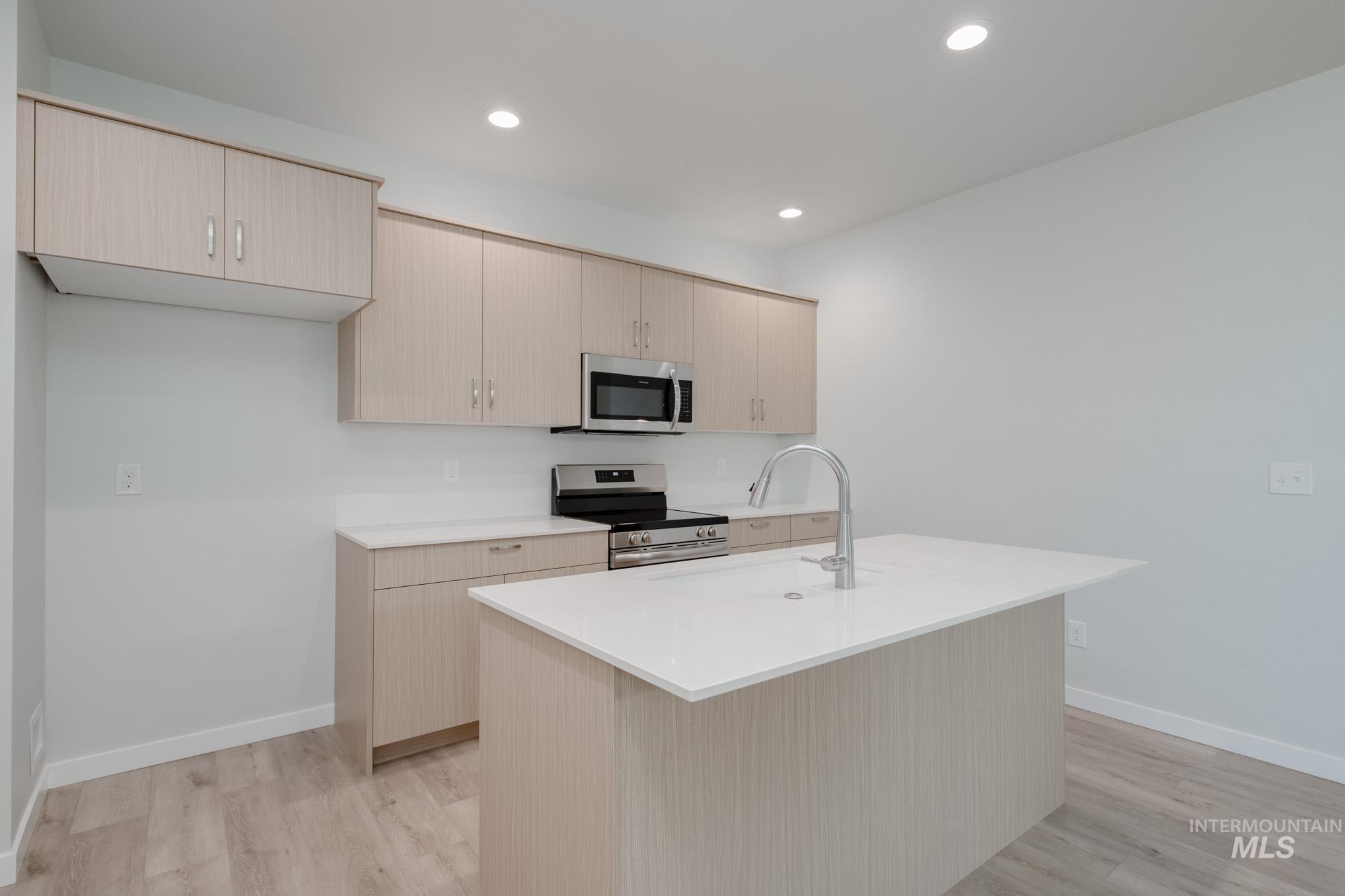 Kitchen featuring appliances with stainless steel finishes, light brown cabinetry, light stone countertops, recessed lighting, and light wood-style floors