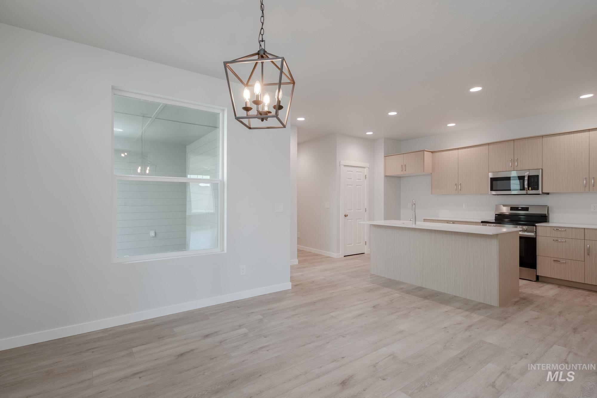 Kitchen featuring light countertops, a kitchen island, appliances with stainless steel finishes, light wood-style flooring, and decorative light fixtures