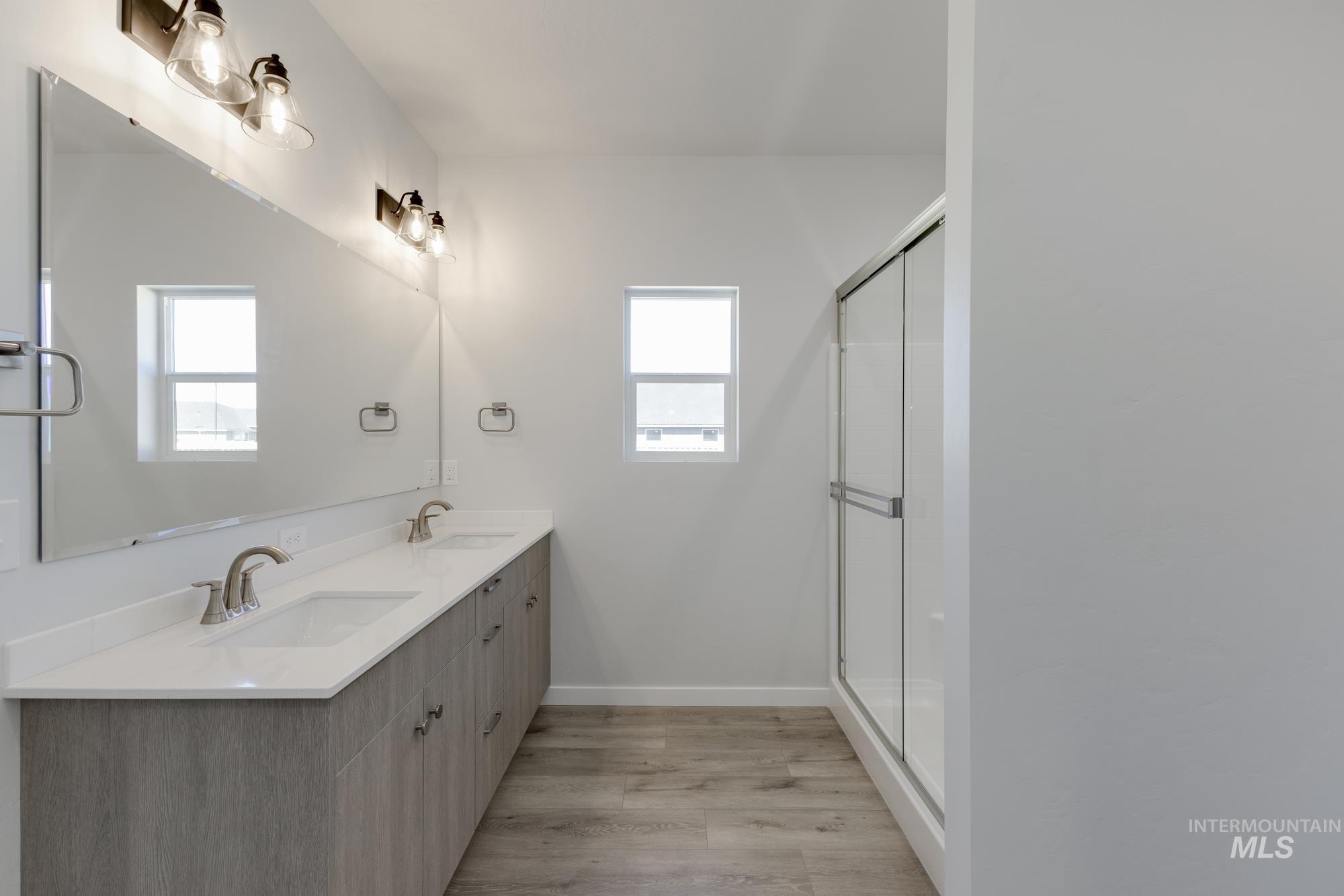 Full bath with light wood finished floors, double vanity, and a shower stall