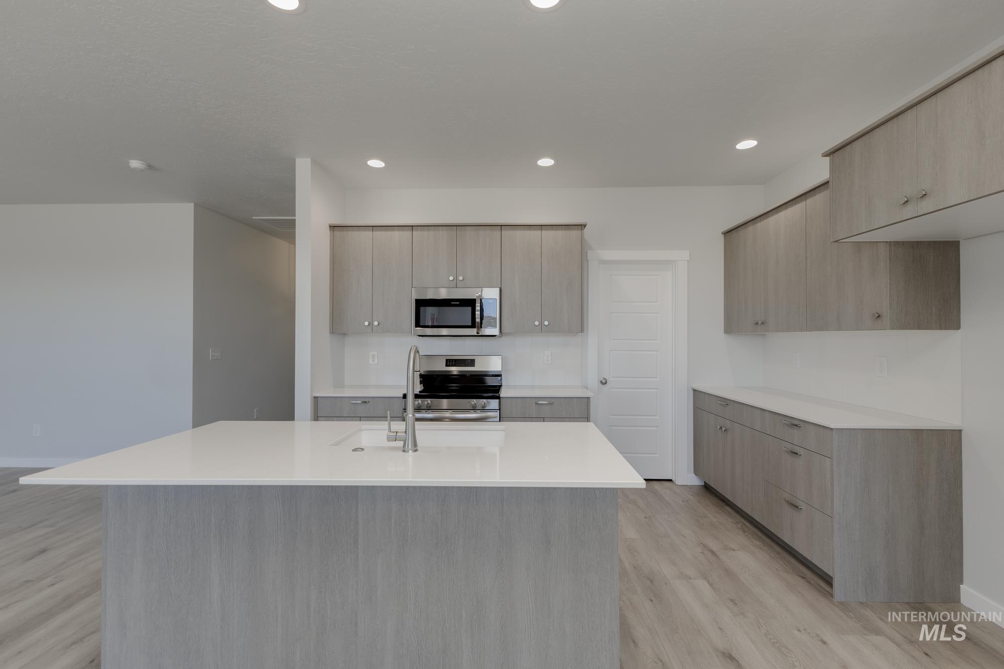 Kitchen with light wood-style floors, a kitchen island with sink, stainless steel appliances, light brown cabinetry, and recessed lighting