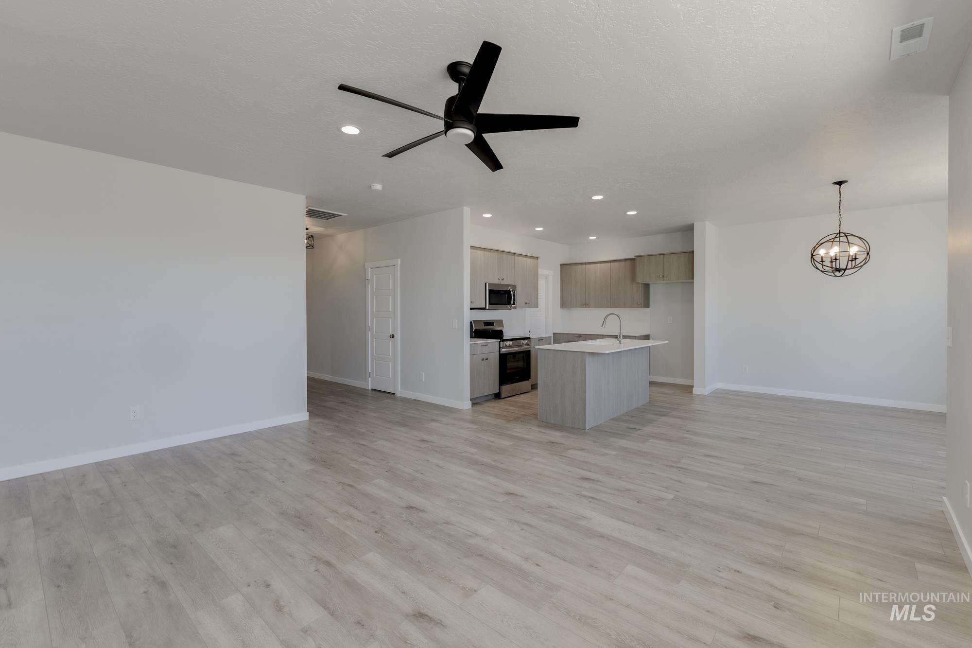 Unfurnished living room featuring a ceiling fan, recessed lighting, light wood-type flooring, and a chandelier