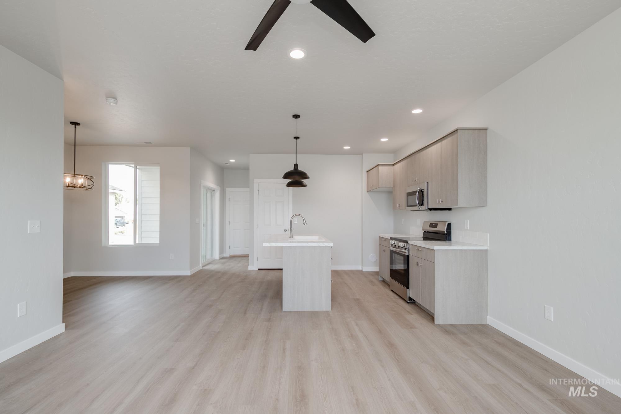 Kitchen with a center island with sink, appliances with stainless steel finishes, light brown cabinetry, light wood finished floors, and decorative light fixtures