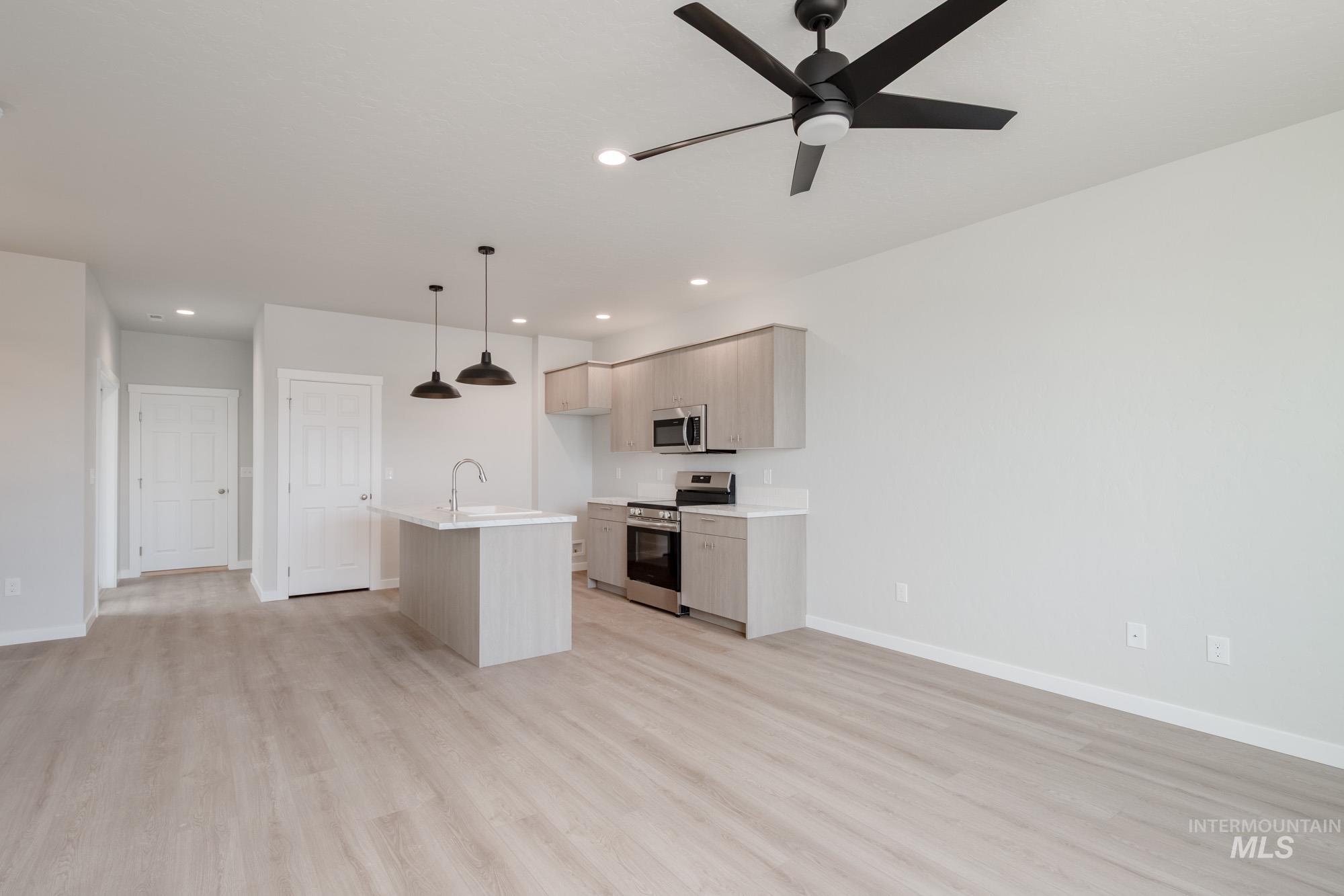 Kitchen featuring an island with sink, appliances with stainless steel finishes, light wood-type flooring, open floor plan, and a kitchen bar