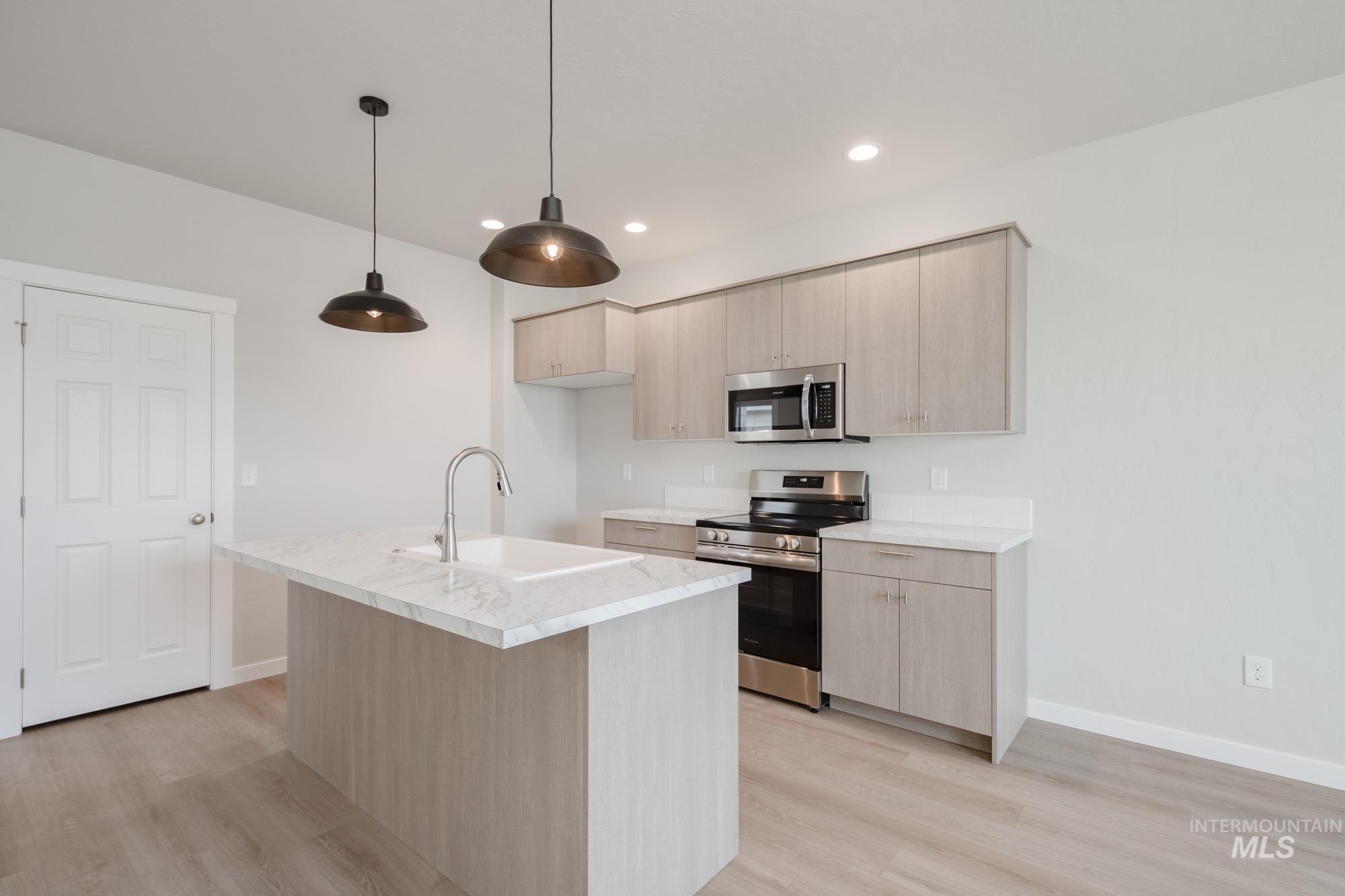 Kitchen featuring light brown cabinets, stainless steel appliances, modern cabinets, light wood-style floors, and a center island with sink