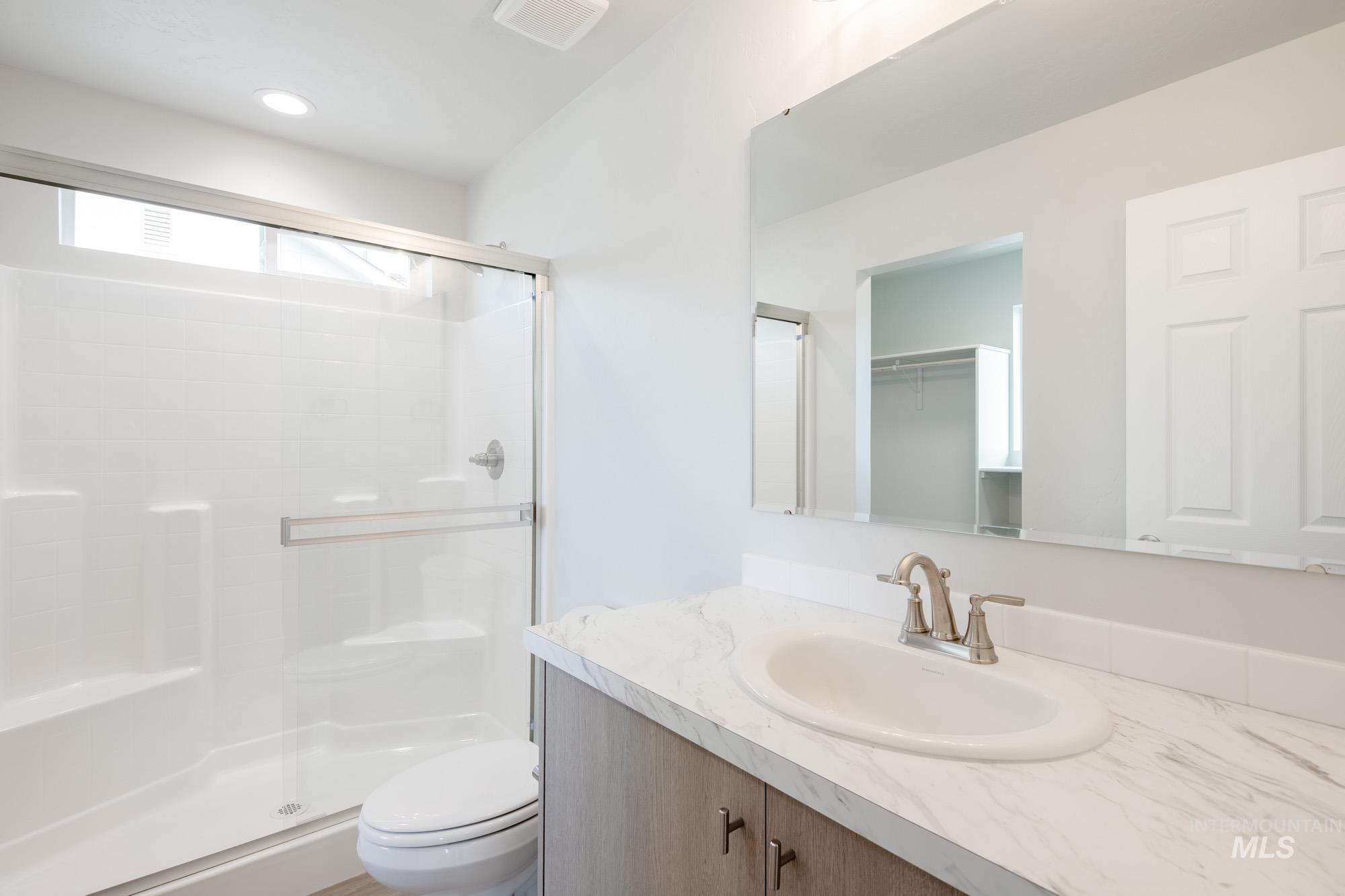 Full bath featuring a stall shower, vanity, a walk in closet, and recessed lighting