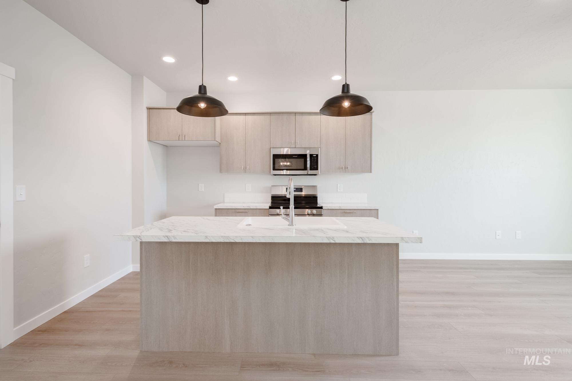 Kitchen with stainless steel appliances, light brown cabinets, light wood-style flooring, hanging light fixtures, and recessed lighting