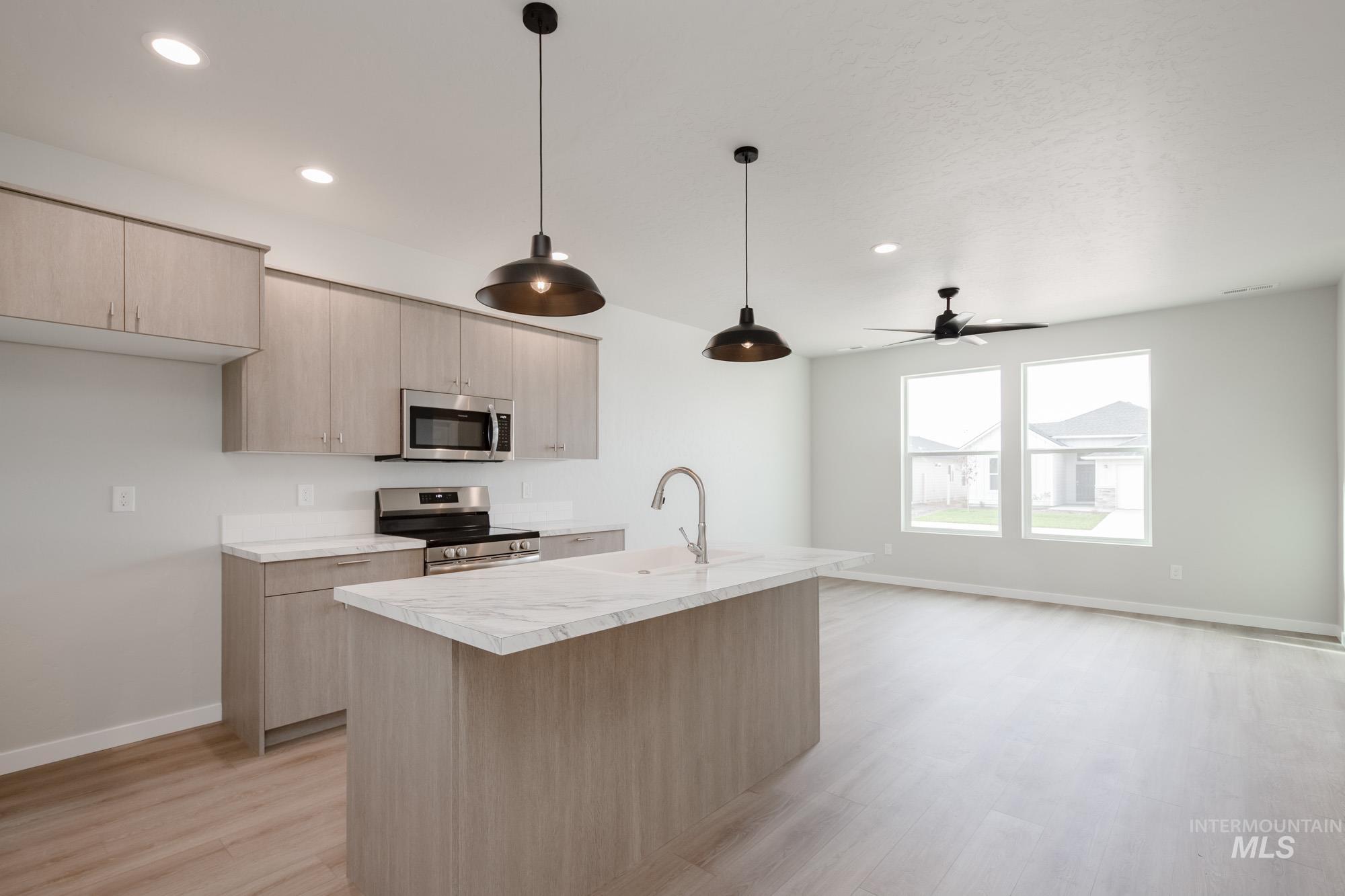 Kitchen with light countertops, hanging light fixtures, stainless steel appliances, a center island with sink, and light brown cabinets