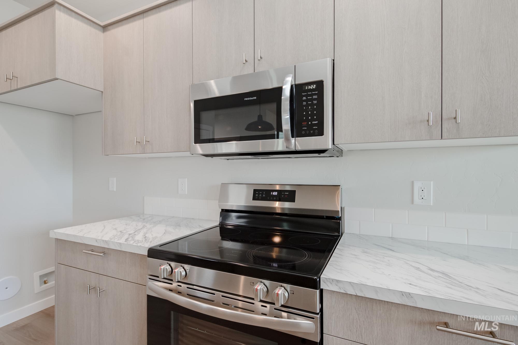 Kitchen featuring appliances with stainless steel finishes, light countertops, light brown cabinetry, light wood-type flooring, and modern cabinets