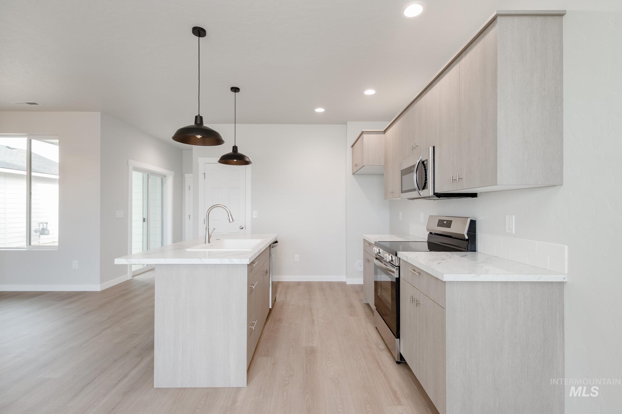 Kitchen featuring light brown cabinets, stainless steel appliances, modern cabinets, light wood finished floors, and an island with sink