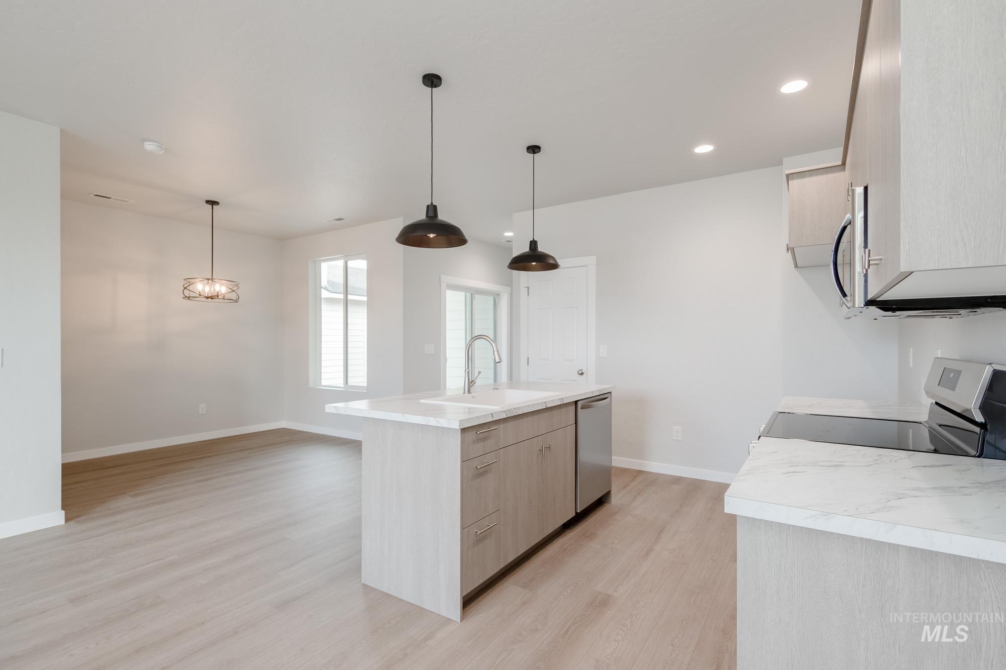 Kitchen featuring light brown cabinets, light countertops, light wood-type flooring, an island with sink, and hanging light fixtures