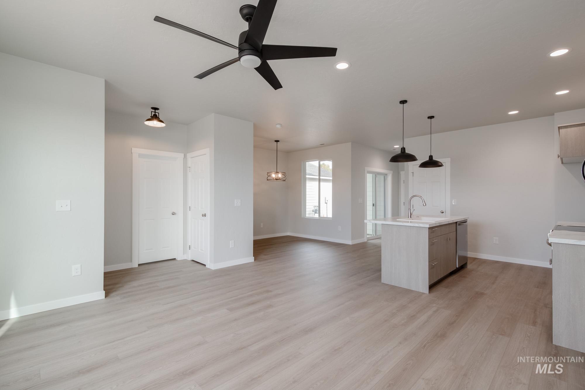 Unfurnished living room featuring light wood-style flooring, a ceiling fan, a chandelier, and recessed lighting