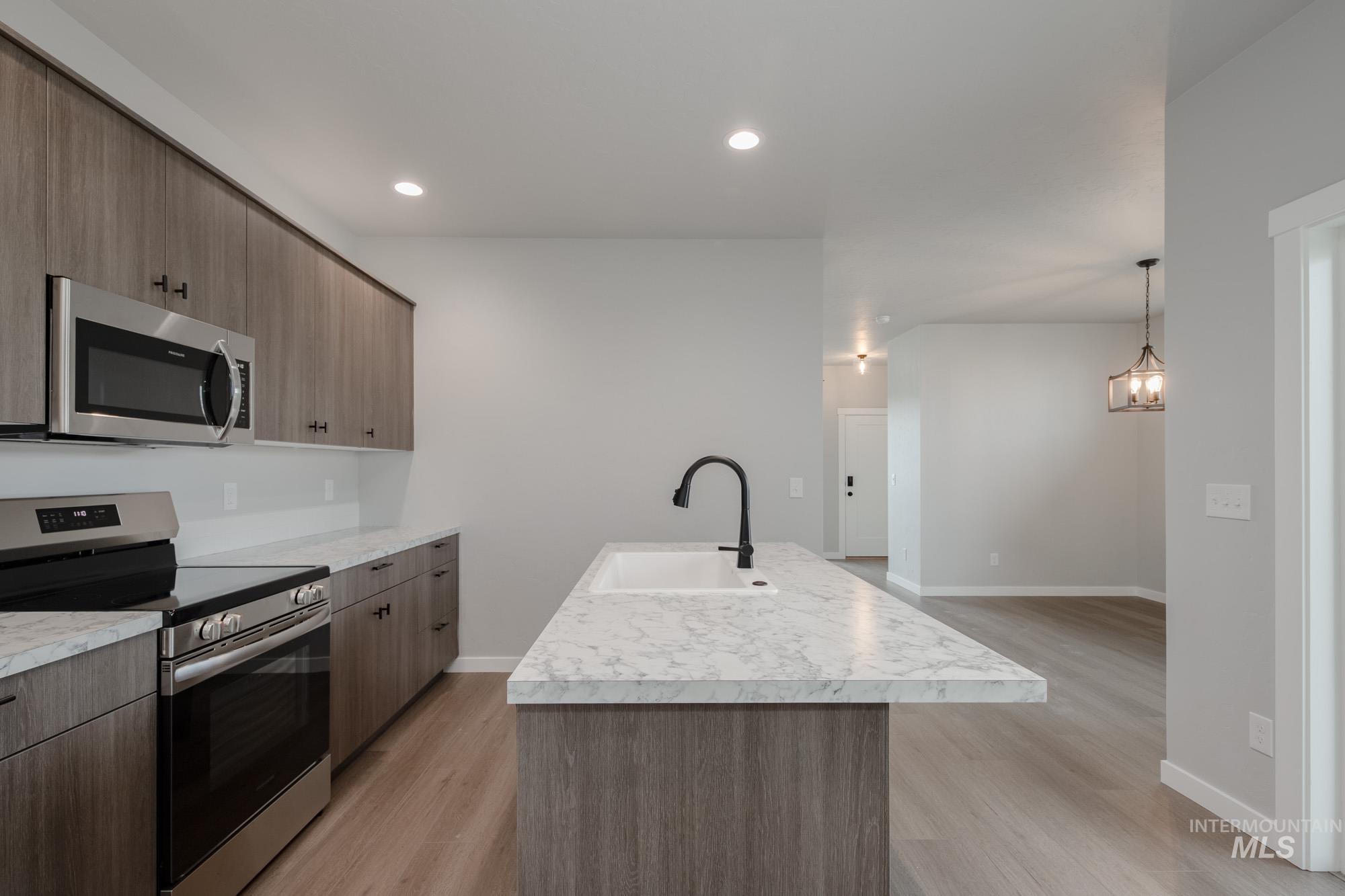 Kitchen with stainless steel appliances, light countertops, a kitchen island with sink, light wood-type flooring, and recessed lighting