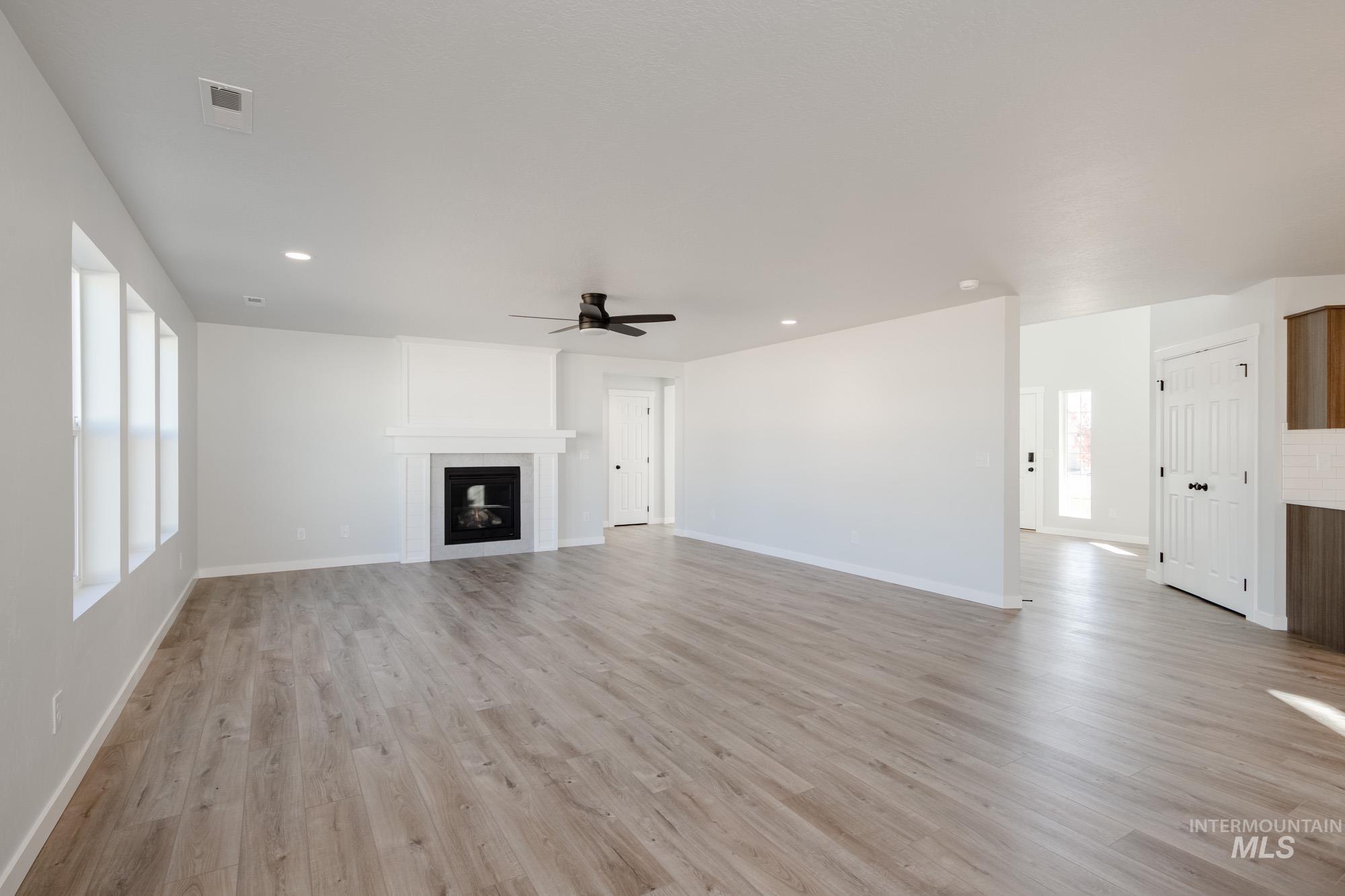 Unfurnished living room featuring a fireplace, ceiling fan, light wood finished floors, and recessed lighting