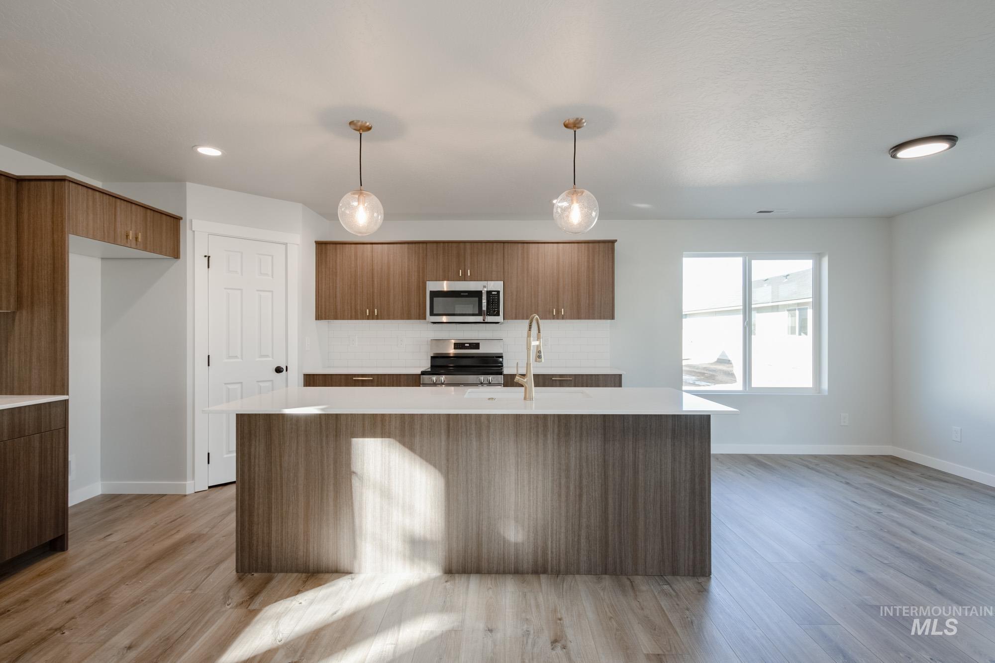 Kitchen featuring a kitchen island with sink, decorative backsplash, decorative light fixtures, appliances with stainless steel finishes, and light wood-style floors