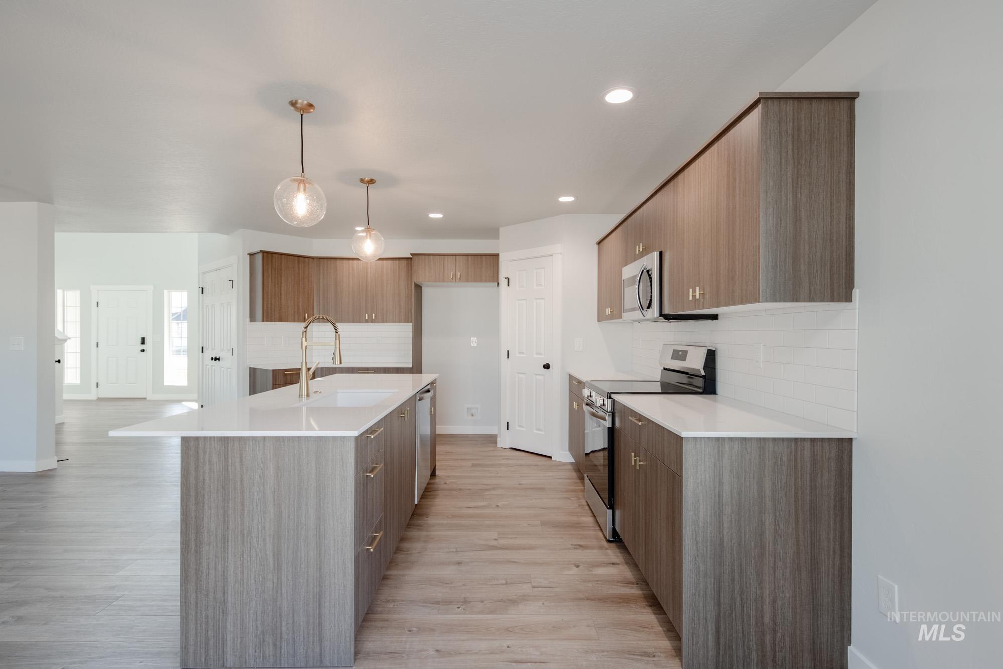 Kitchen featuring modern cabinets, stainless steel appliances, backsplash, decorative light fixtures, and a kitchen island with sink