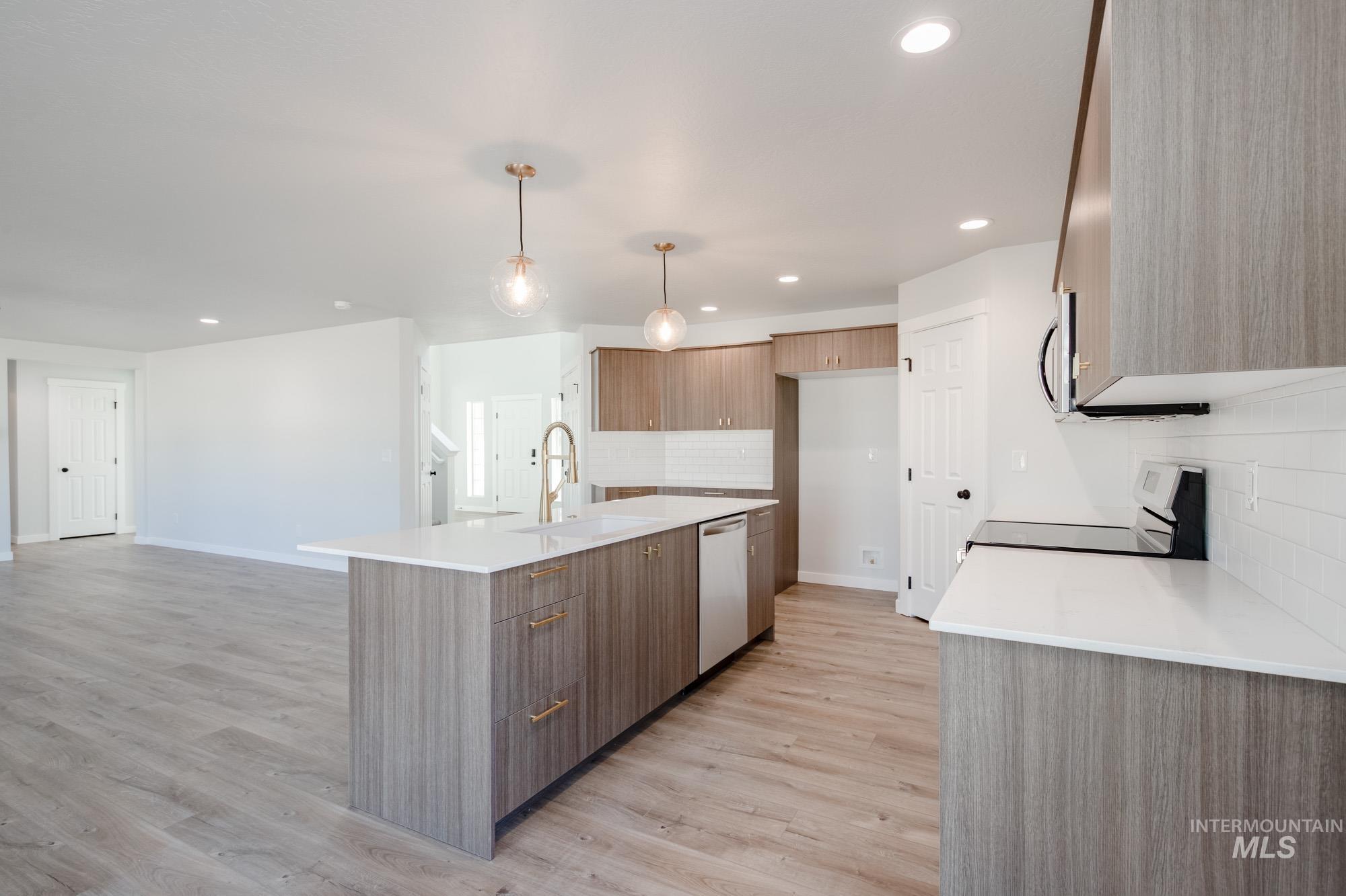 Kitchen featuring modern cabinets, appliances with stainless steel finishes, light stone counters, light wood-style floors, and a kitchen island with sink