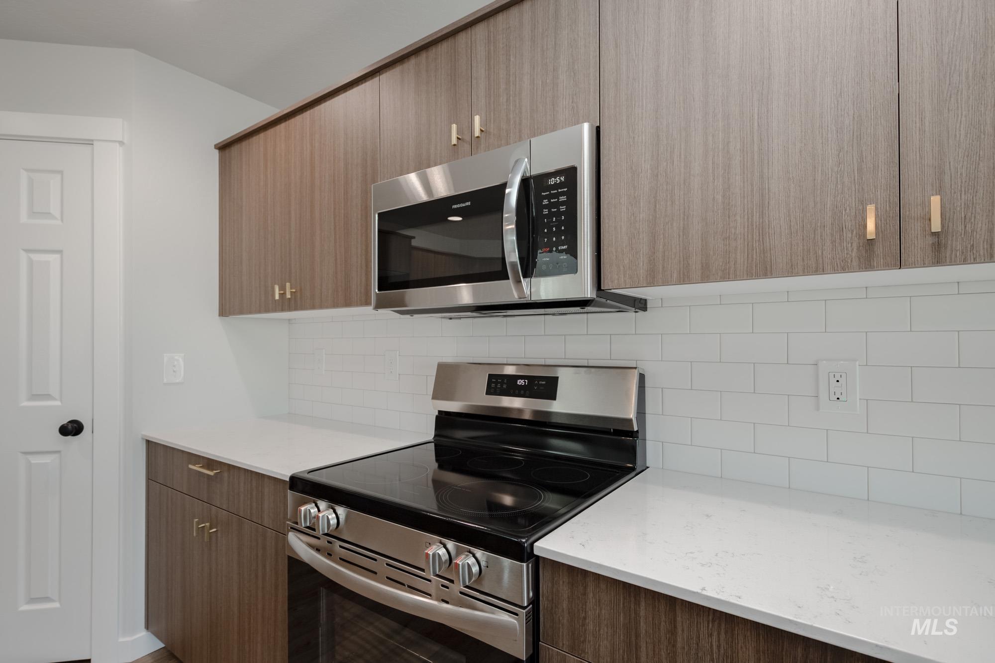 Kitchen with stainless steel appliances, modern cabinets, backsplash, and light stone countertops
