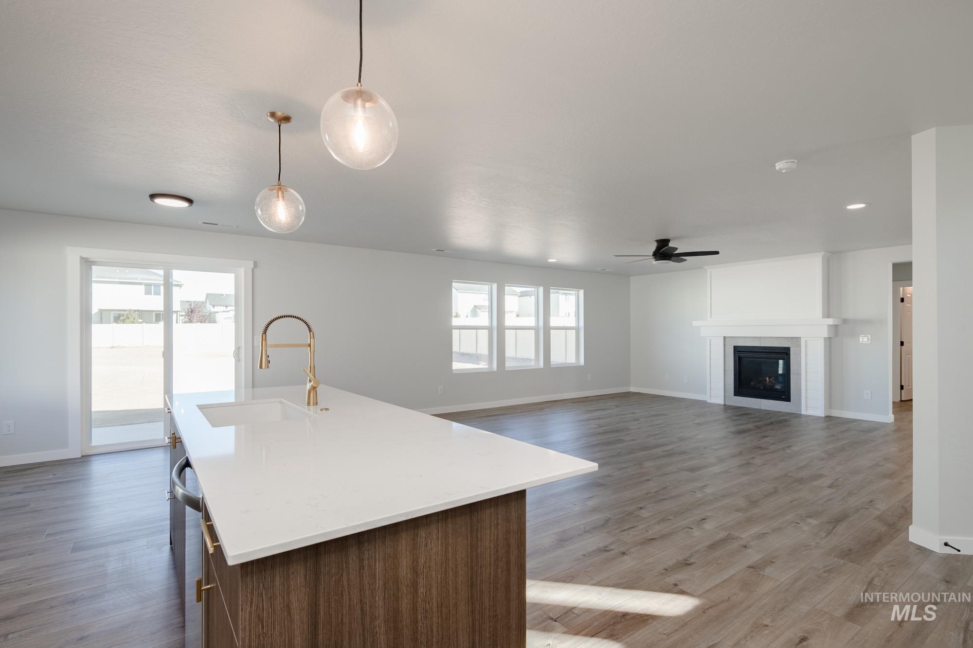 Kitchen featuring open floor plan, an island with sink, pendant lighting, a tiled fireplace, and light stone counters