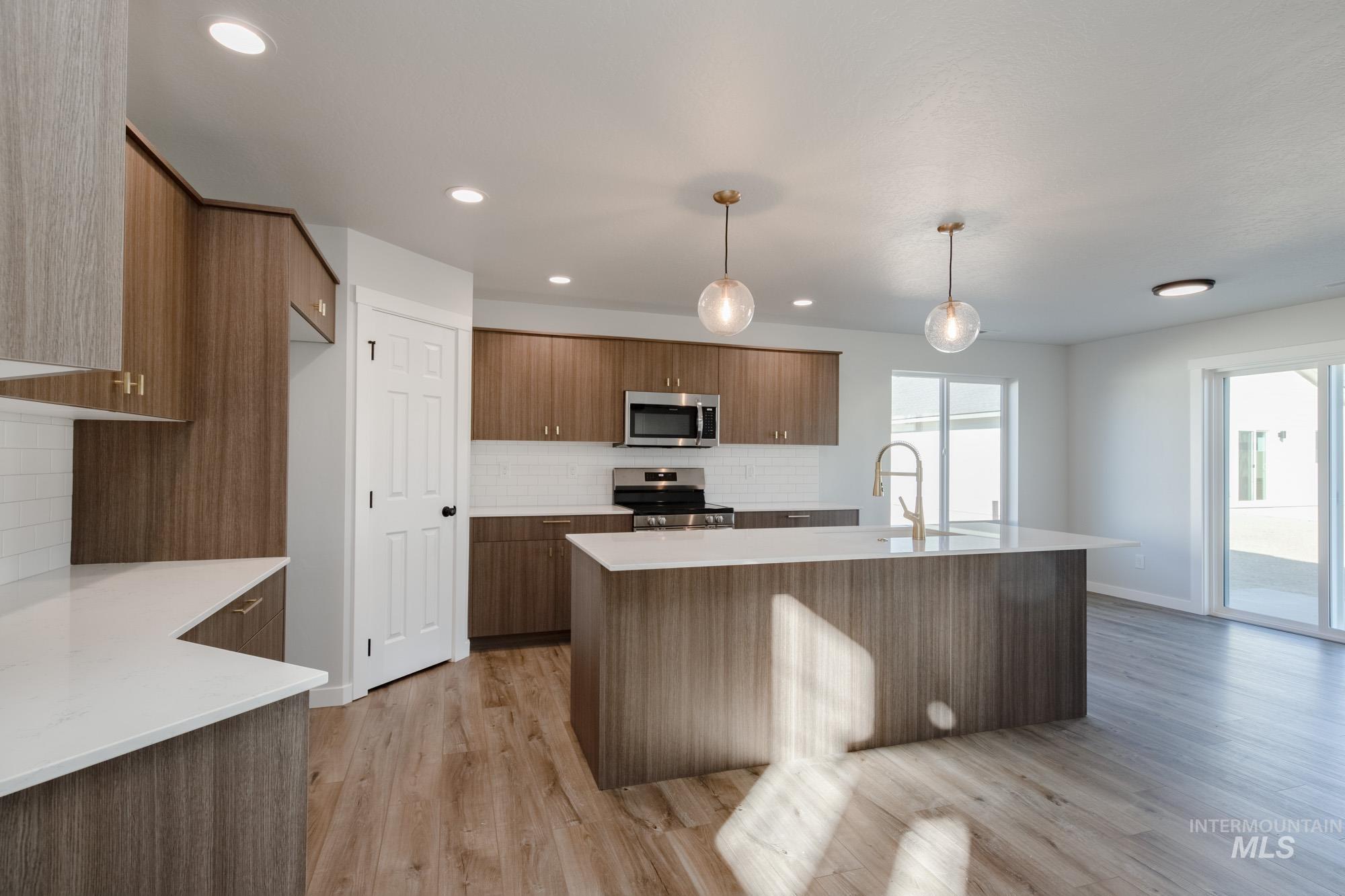 Kitchen with hanging light fixtures, appliances with stainless steel finishes, light stone counters, tasteful backsplash, and recessed lighting