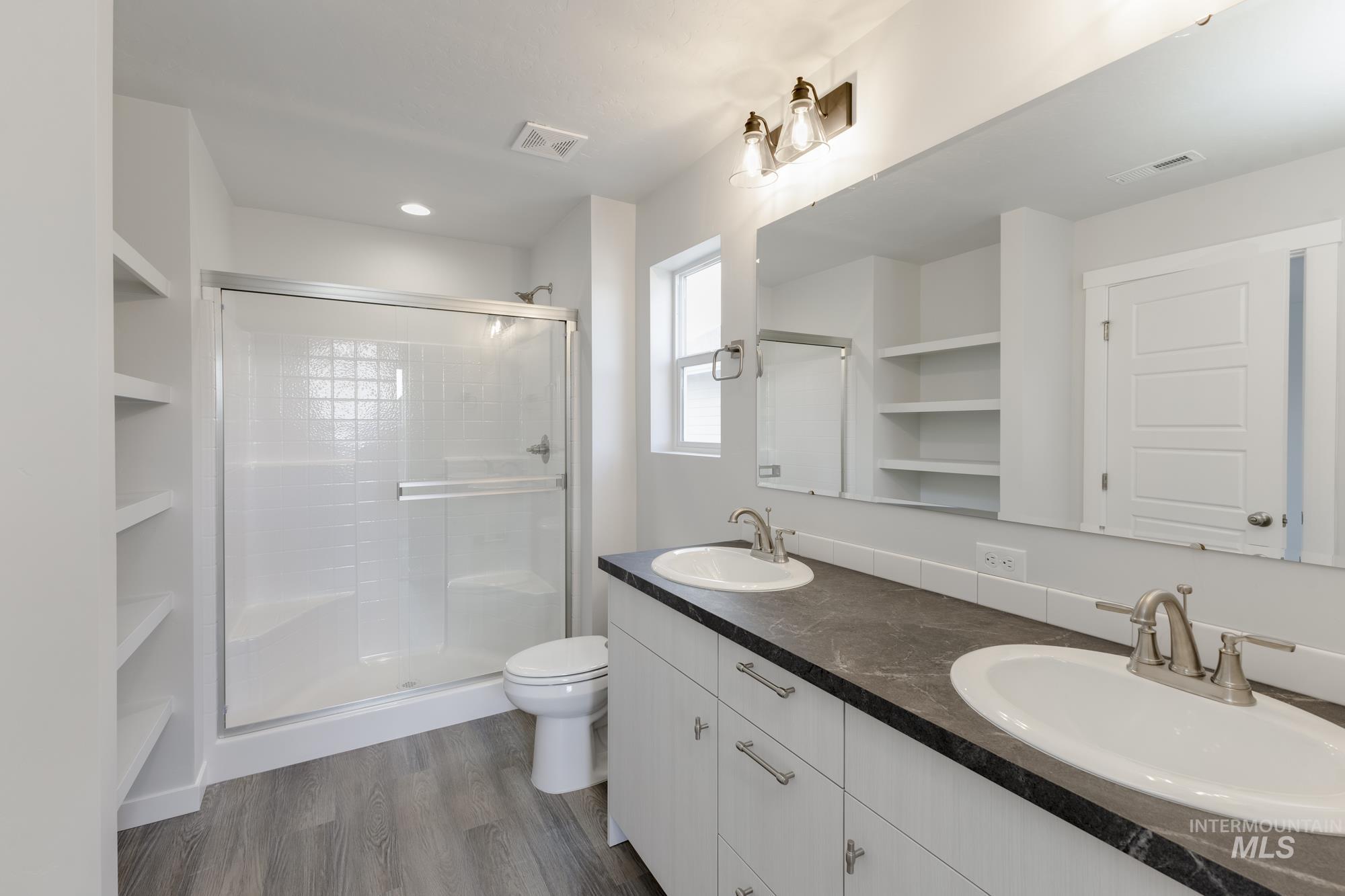 Bathroom featuring a shower stall, double vanity, dark wood-style floors, built in shelves, and recessed lighting