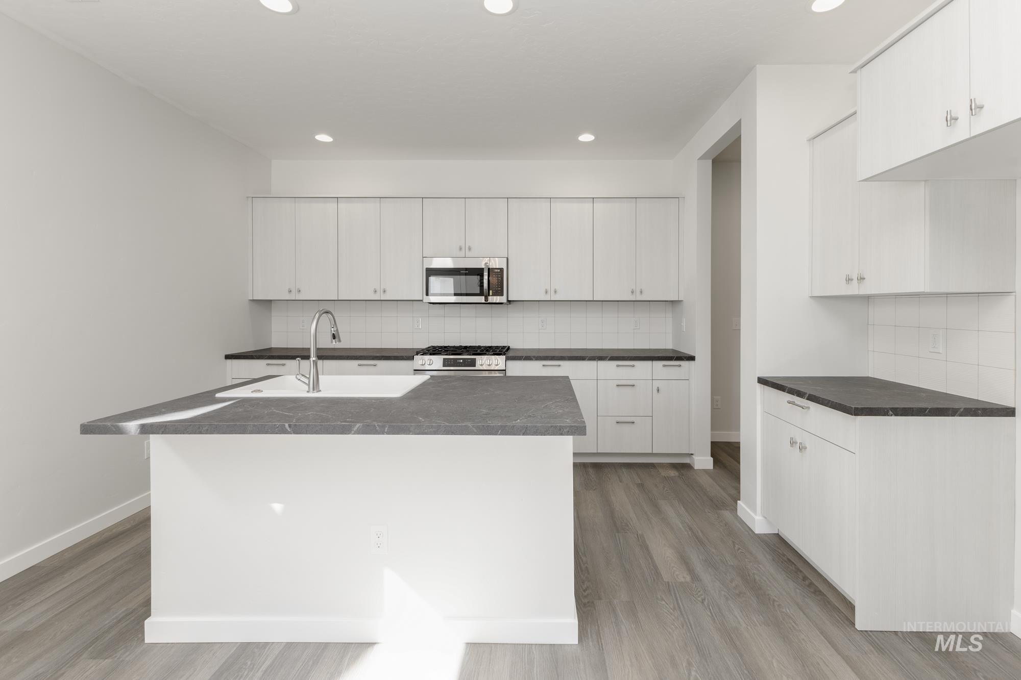 Kitchen with decorative backsplash, a kitchen island with sink, white cabinets, and recessed lighting
