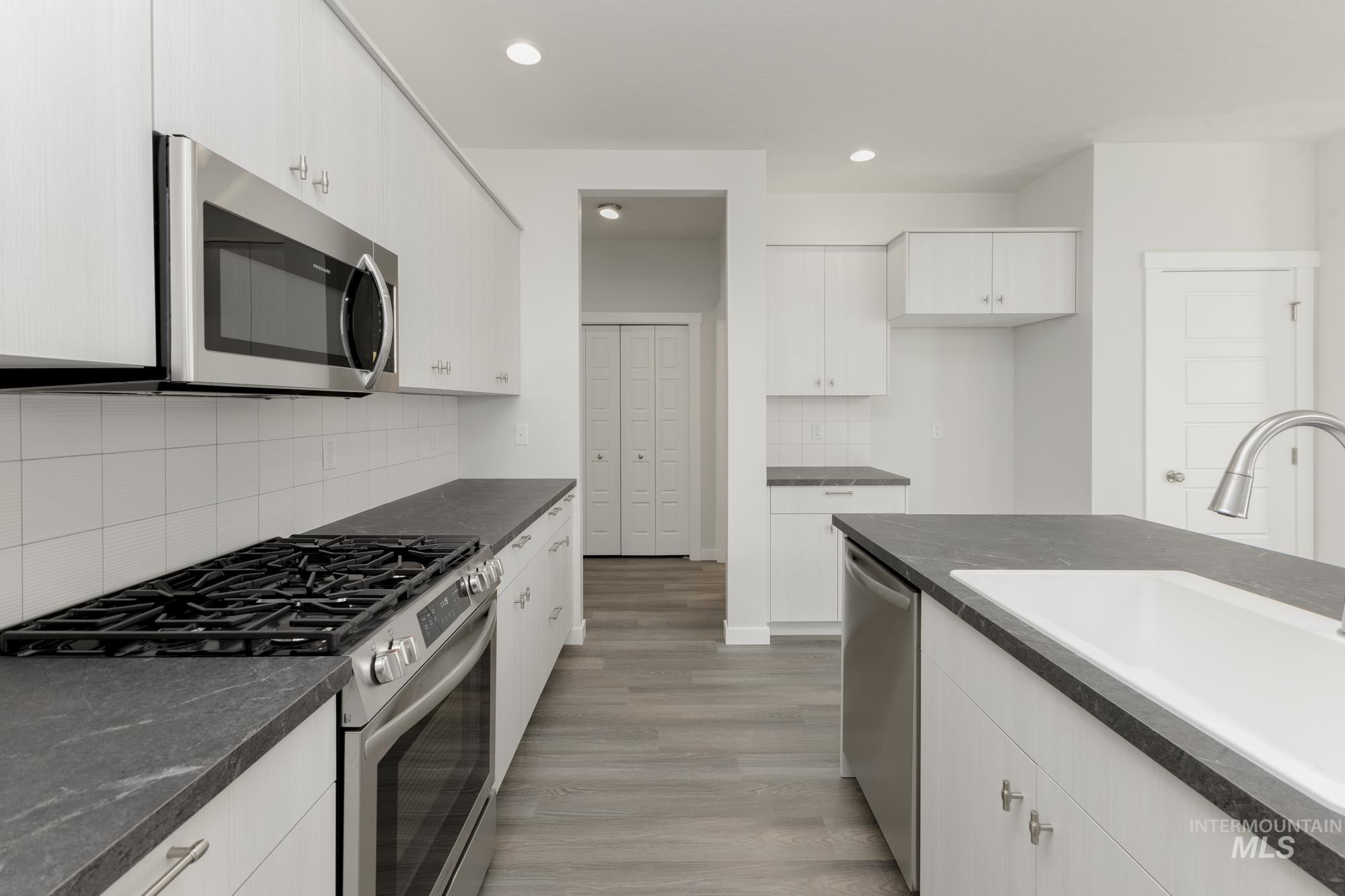 Kitchen with stainless steel appliances, tasteful backsplash, light wood-style flooring, recessed lighting, and white cabinetry