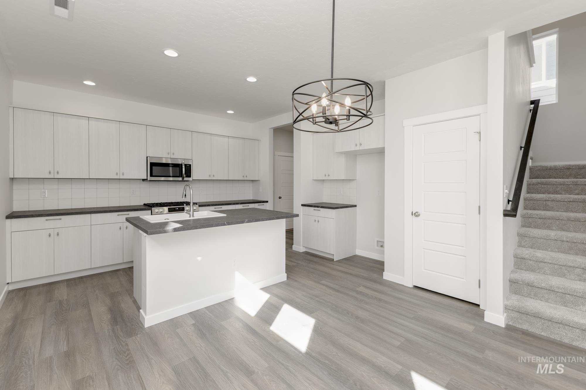 Kitchen featuring decorative backsplash, white cabinets, pendant lighting, a center island with sink, and appliances with stainless steel finishes