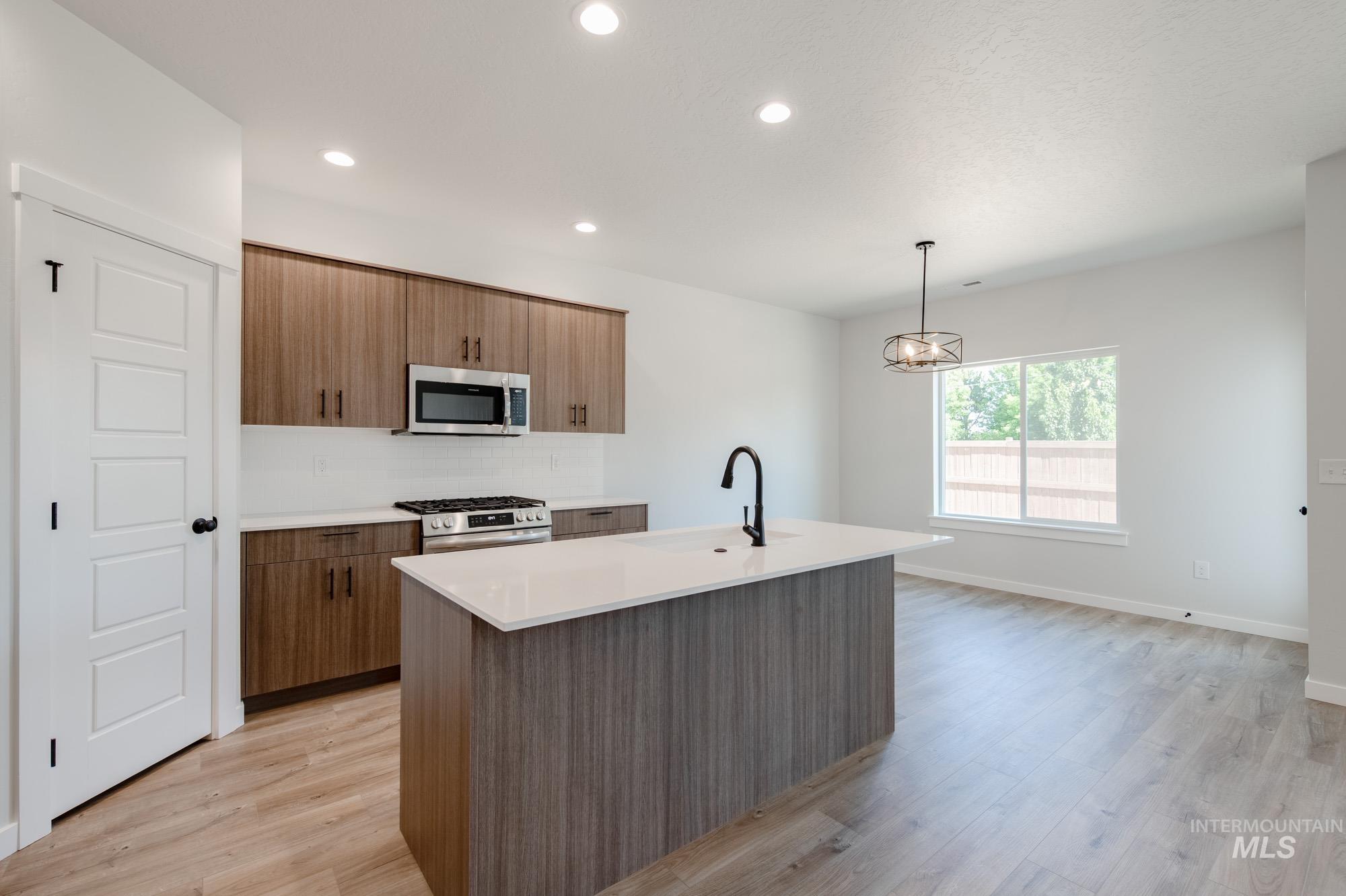 Kitchen with hanging light fixtures, stainless steel appliances, a kitchen island with sink, recessed lighting, and light wood-style floors