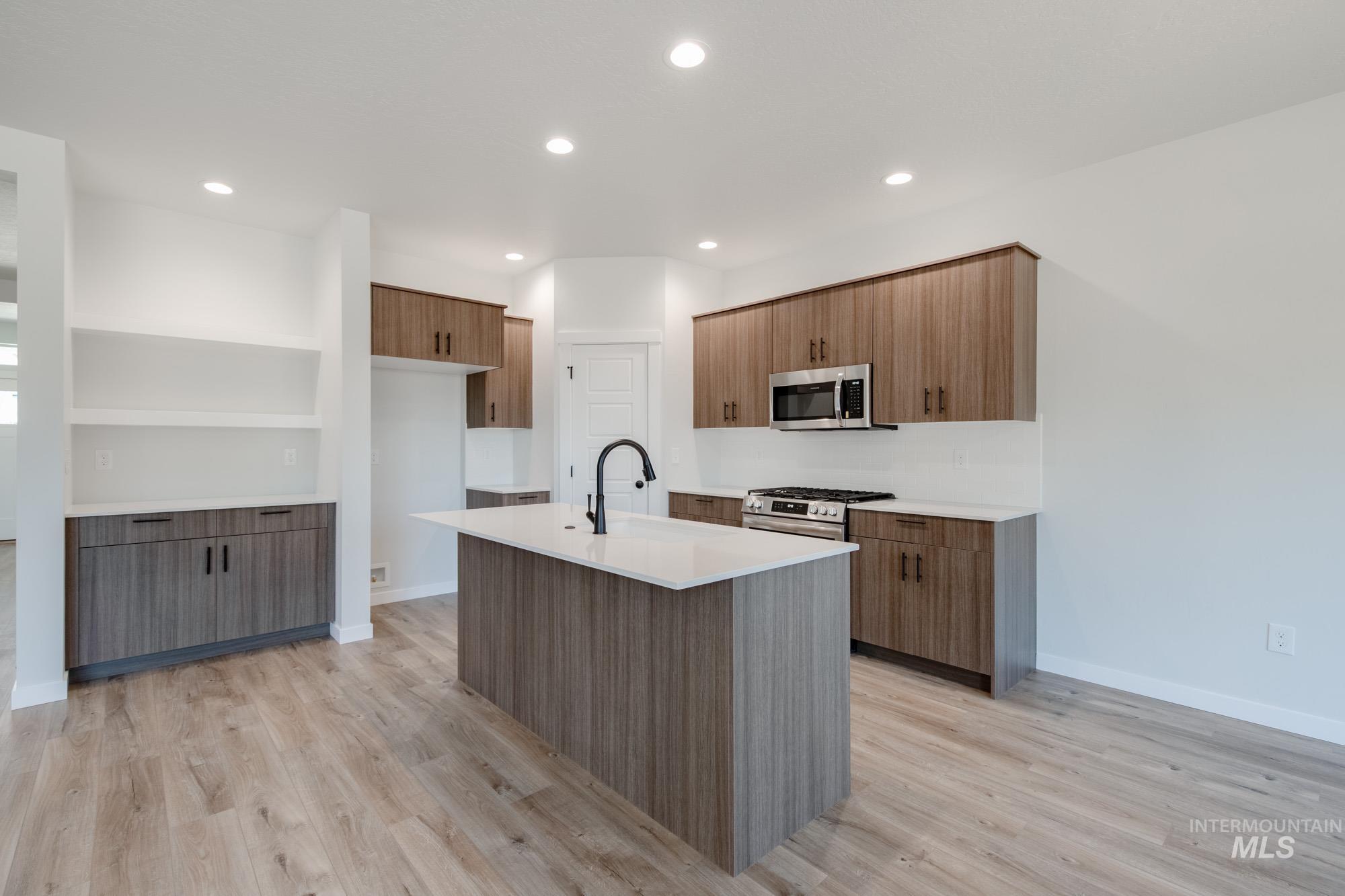 Kitchen with a kitchen island with sink, light stone counters, light wood finished floors, stainless steel appliances, and recessed lighting