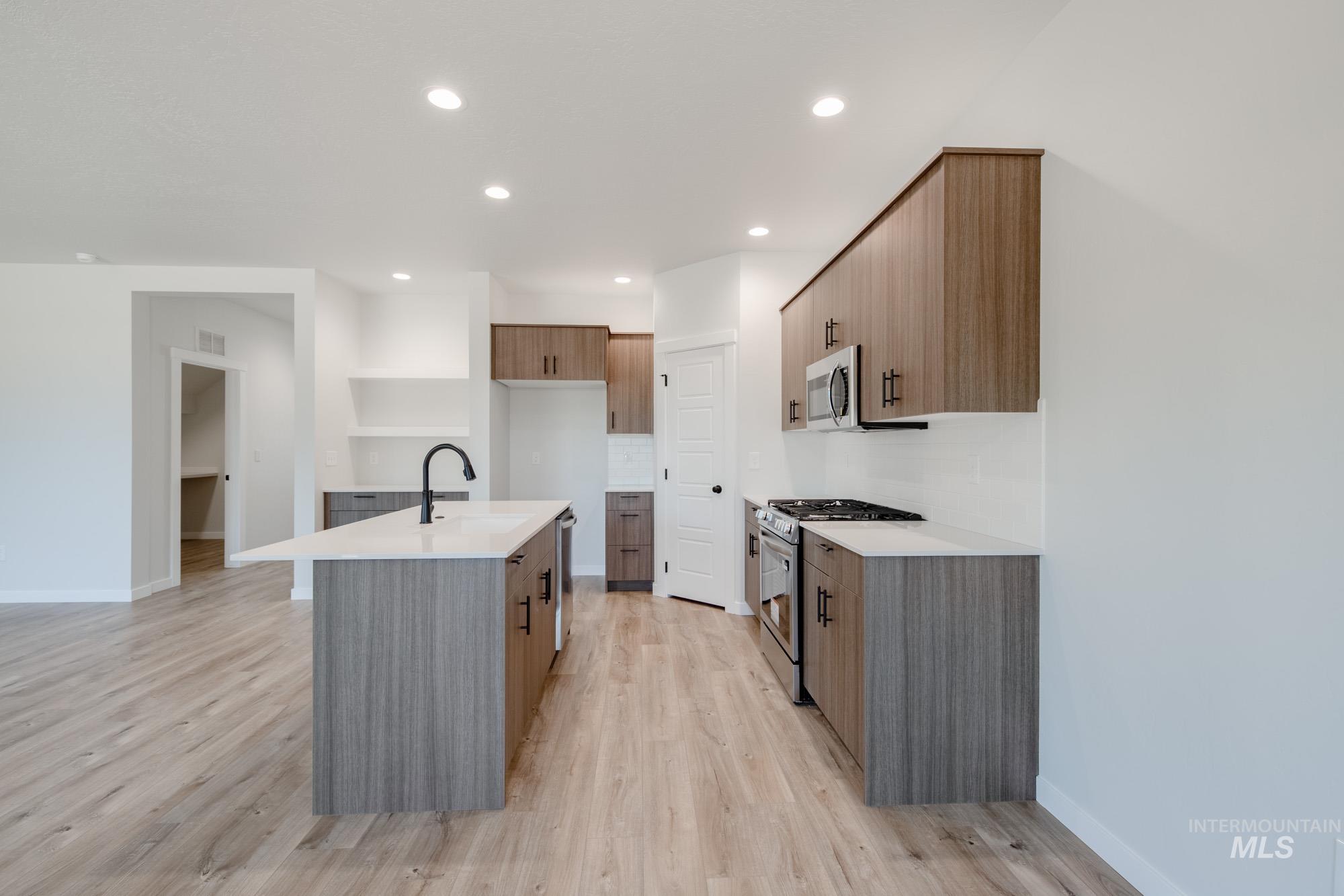 Kitchen with stainless steel appliances, a kitchen island with sink, light wood-style floors, recessed lighting, and light stone countertops