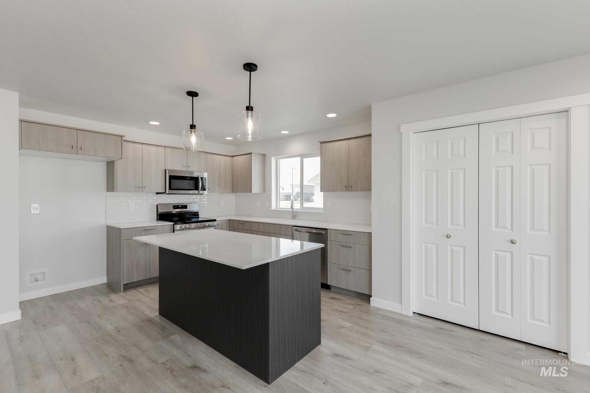 Kitchen with modern cabinets, backsplash, a kitchen island, decorative light fixtures, and stainless steel appliances