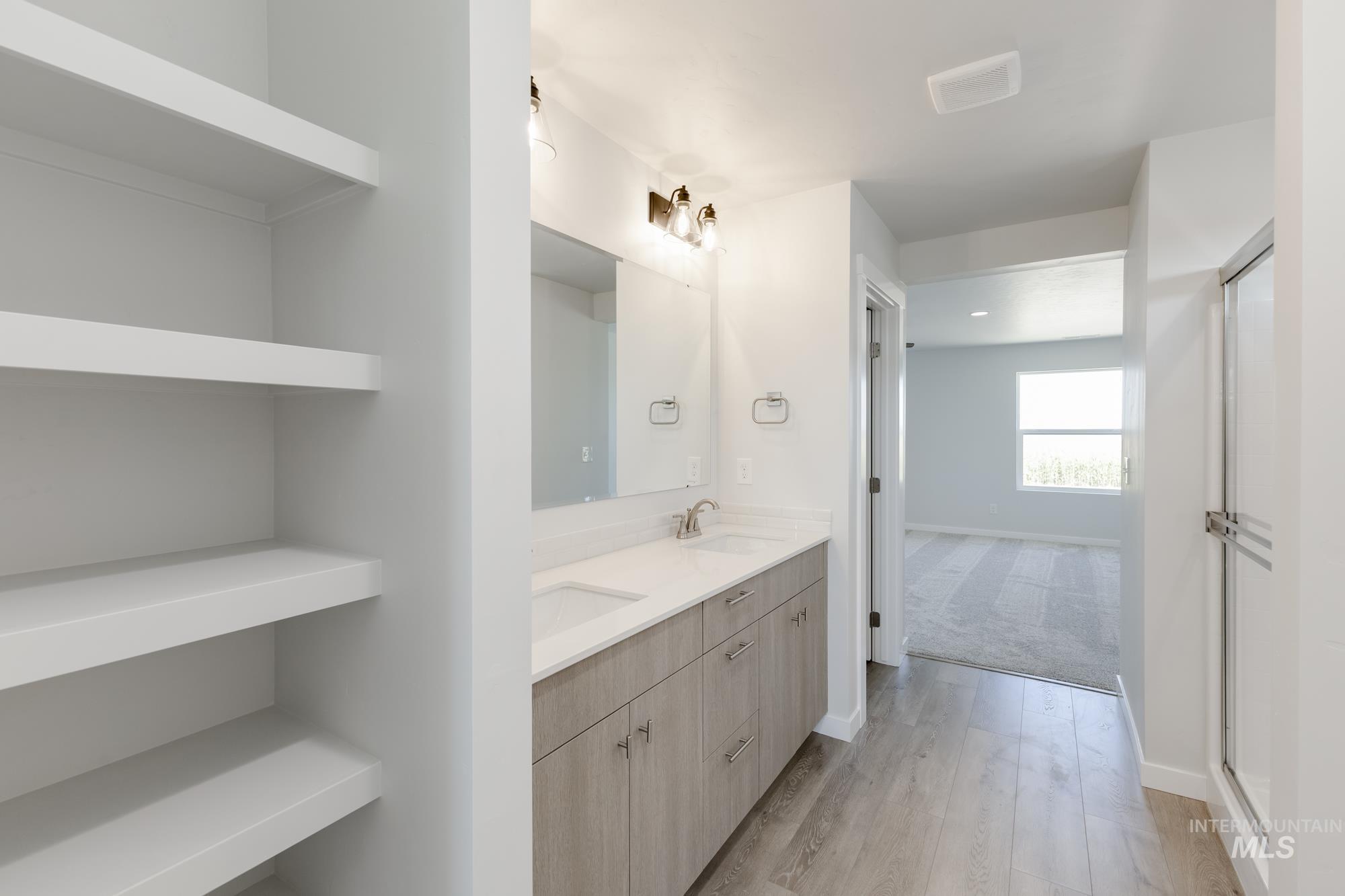 Full bathroom with double vanity, light wood-style flooring, and a shower with door