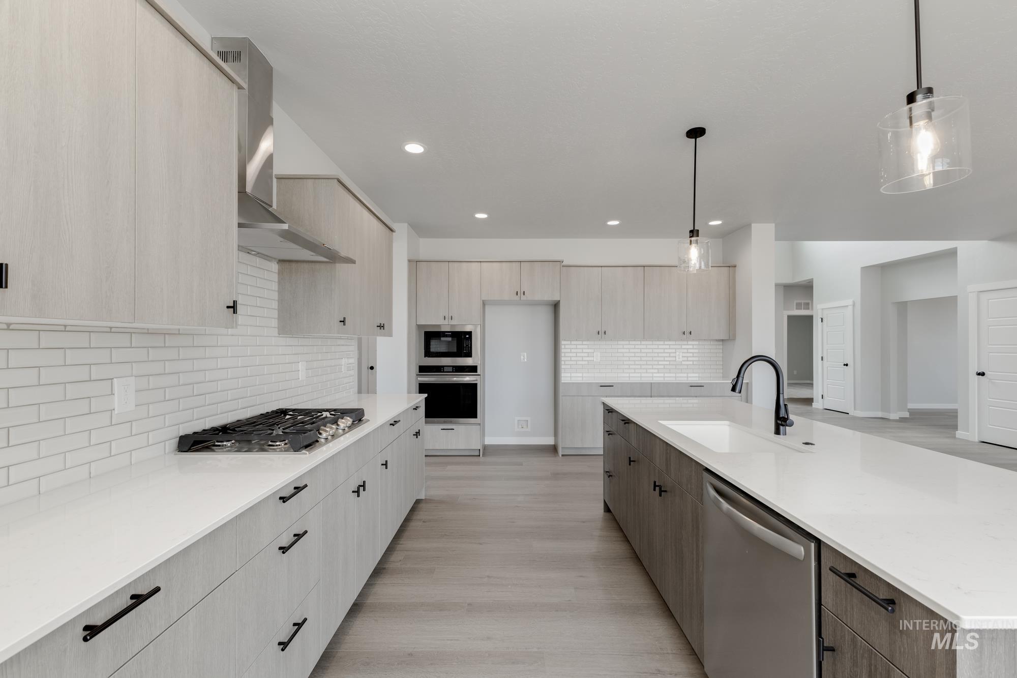 Kitchen with modern cabinets, appliances with stainless steel finishes, pendant lighting, light stone counters, and light brown cabinets