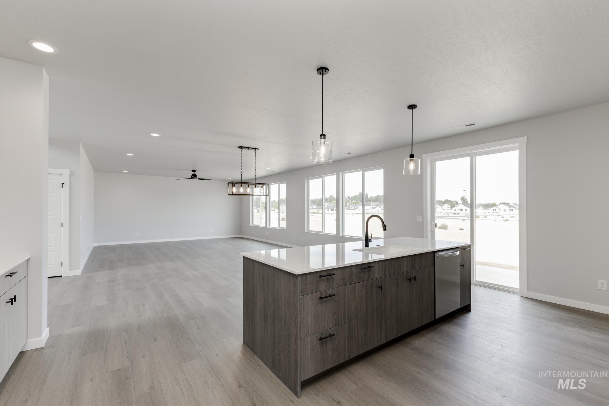 Kitchen with light wood-type flooring, ceiling fan, pendant lighting, an island with sink, and recessed lighting