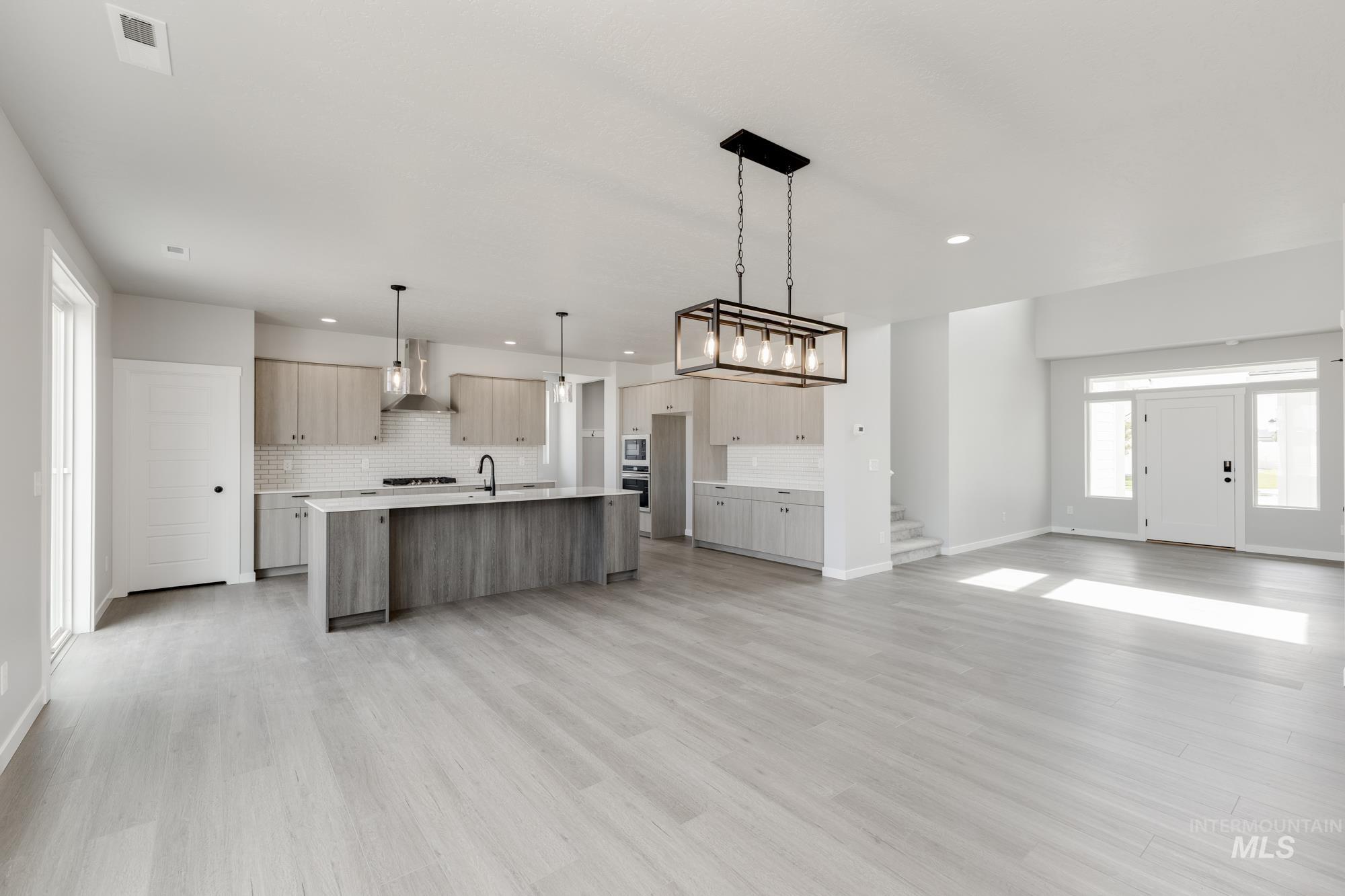 Kitchen featuring open floor plan, a center island with sink, decorative backsplash, and hanging light fixtures