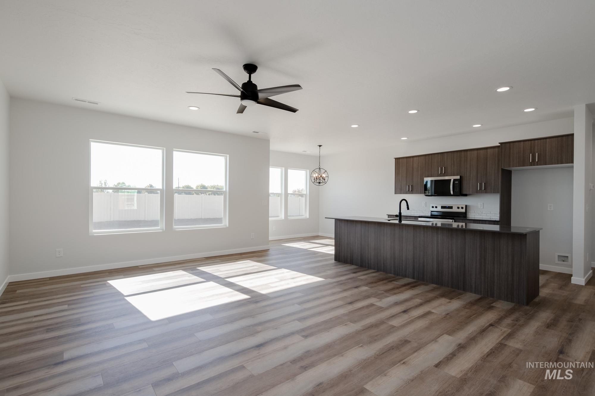 Kitchen featuring open floor plan, dark brown cabinets, dark countertops, a kitchen island with sink, and a ceiling fan