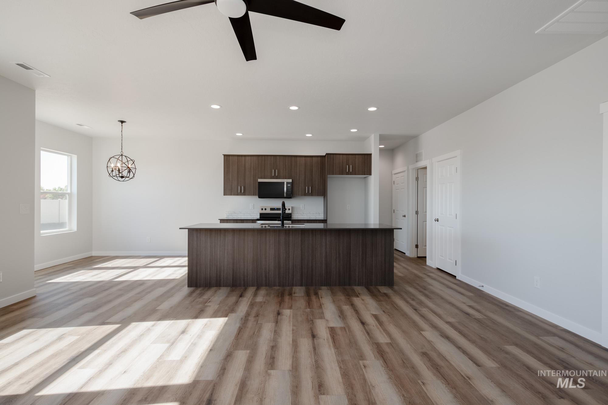 Kitchen featuring open floor plan, dark brown cabinets, light wood-style floors, an island with sink, and recessed lighting
