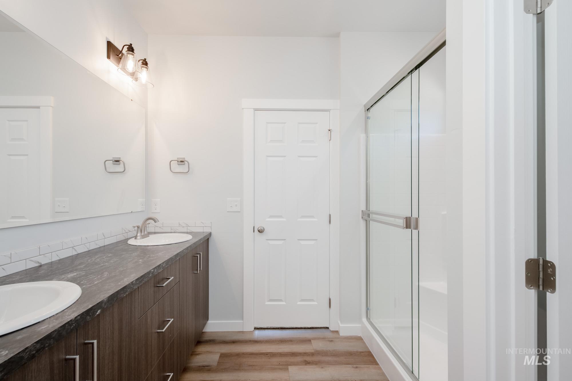 Bathroom featuring light wood-type flooring, double vanity, and a stall shower