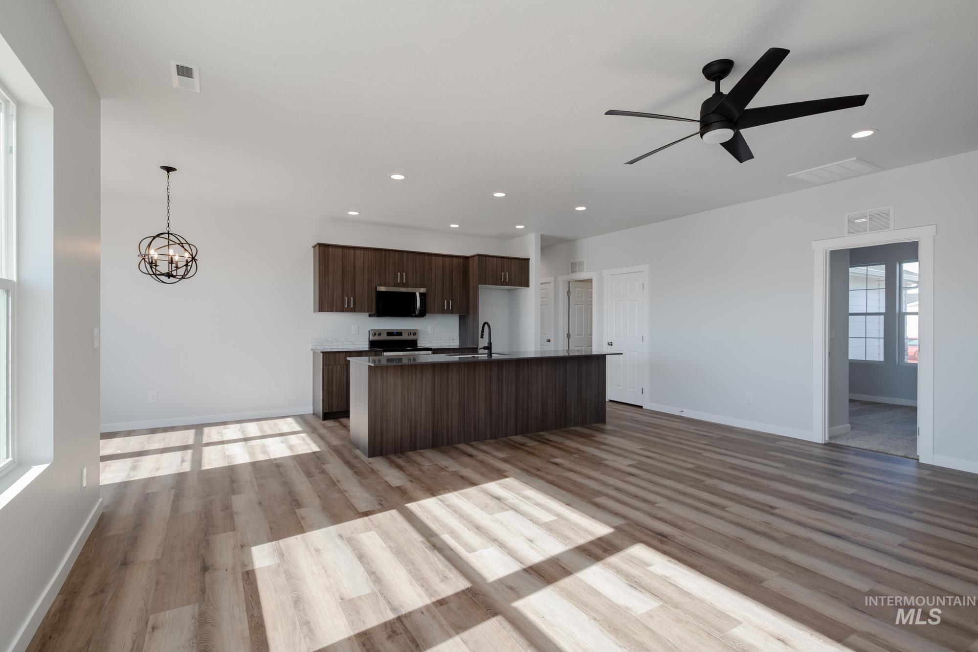 Kitchen featuring open floor plan, dark brown cabinetry, light wood finished floors, dark countertops, and recessed lighting