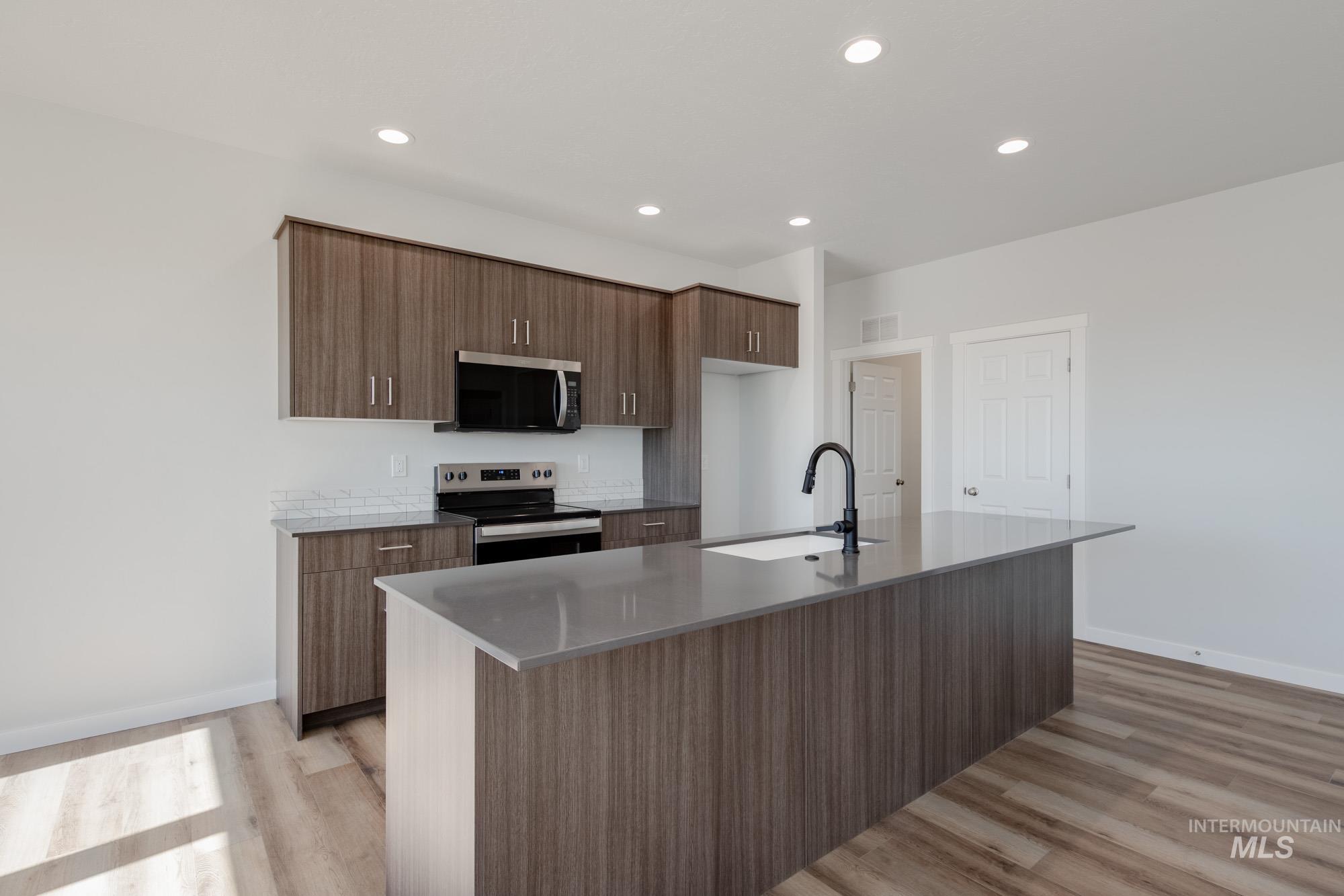 Kitchen featuring an island with sink, stainless steel appliances, recessed lighting, light wood finished floors, and light stone countertops