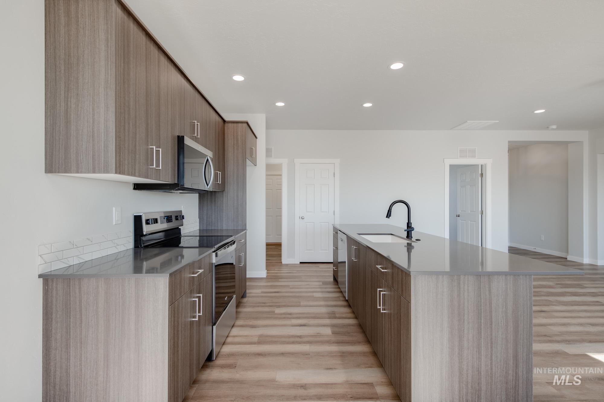 Kitchen featuring modern cabinets, appliances with stainless steel finishes, recessed lighting, light wood finished floors, and dark stone counters