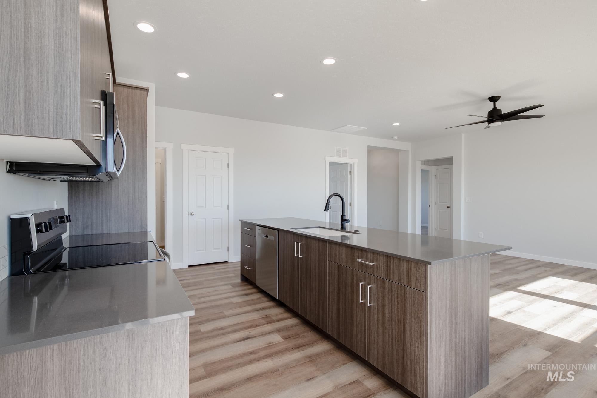 Kitchen with recessed lighting, modern cabinets, stainless steel appliances, light wood-type flooring, and an island with sink