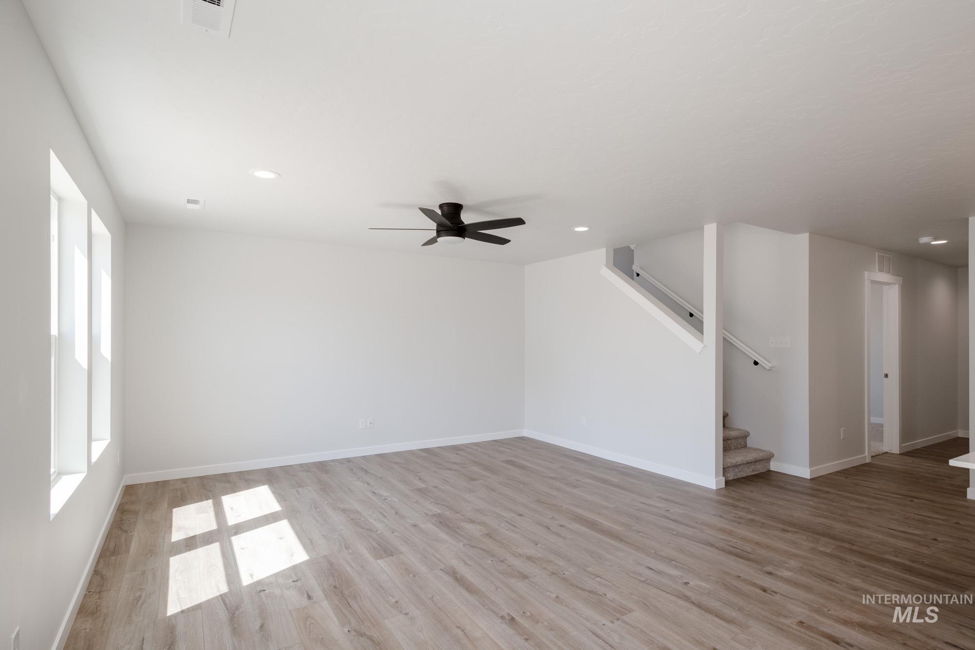 Unfurnished living room with a ceiling fan, light wood-type flooring, recessed lighting, and stairway