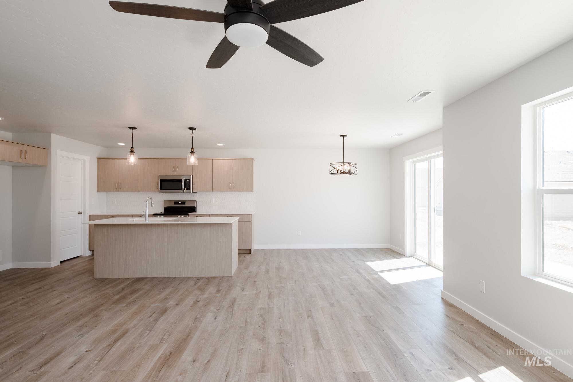 Kitchen featuring light countertops, an island with sink, decorative light fixtures, and light wood-style floors