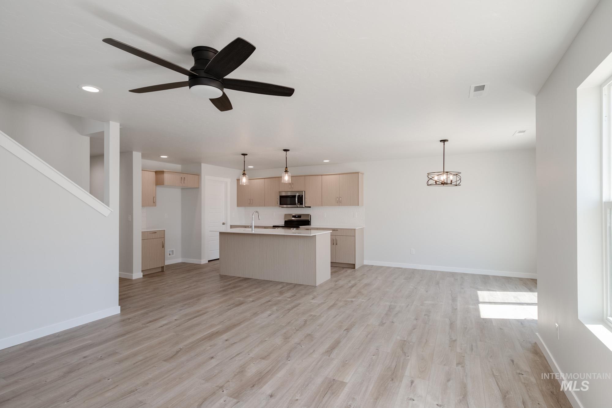 Kitchen featuring open floor plan, hanging light fixtures, a center island with sink, light wood finished floors, and ceiling fan
