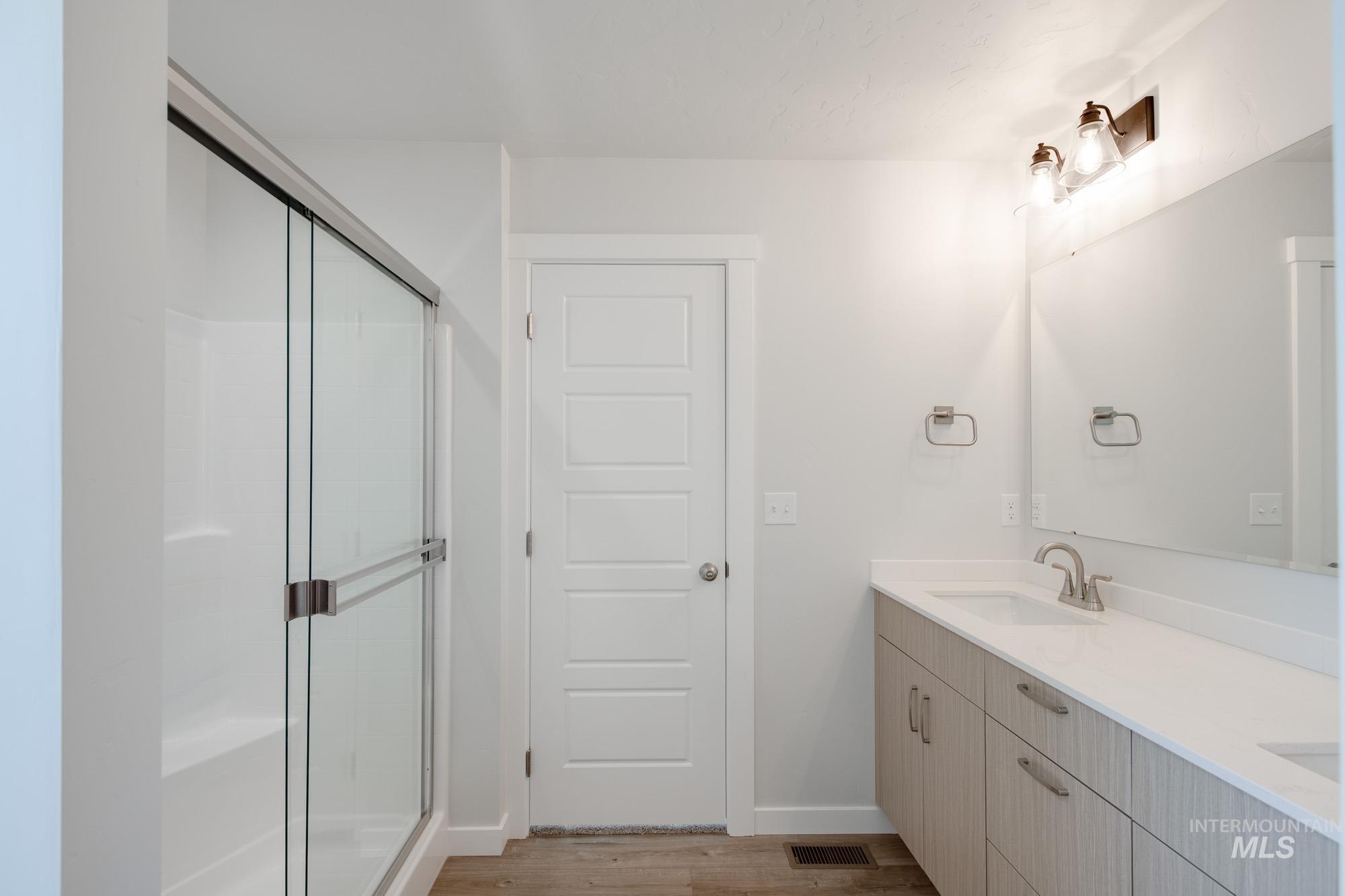 Bathroom featuring light wood finished floors, a stall shower, and double vanity